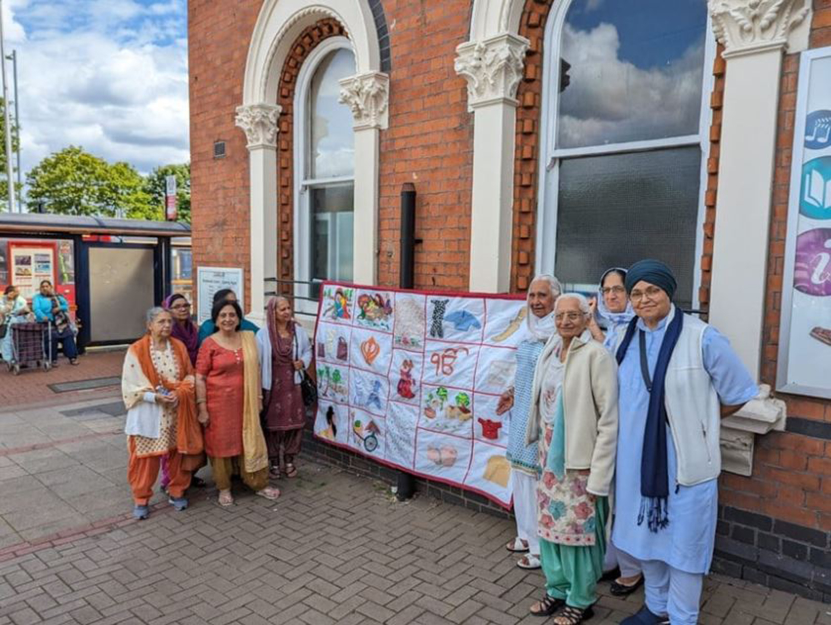 A group photograph of Sikh project participants showcasing an embroidered tapestry