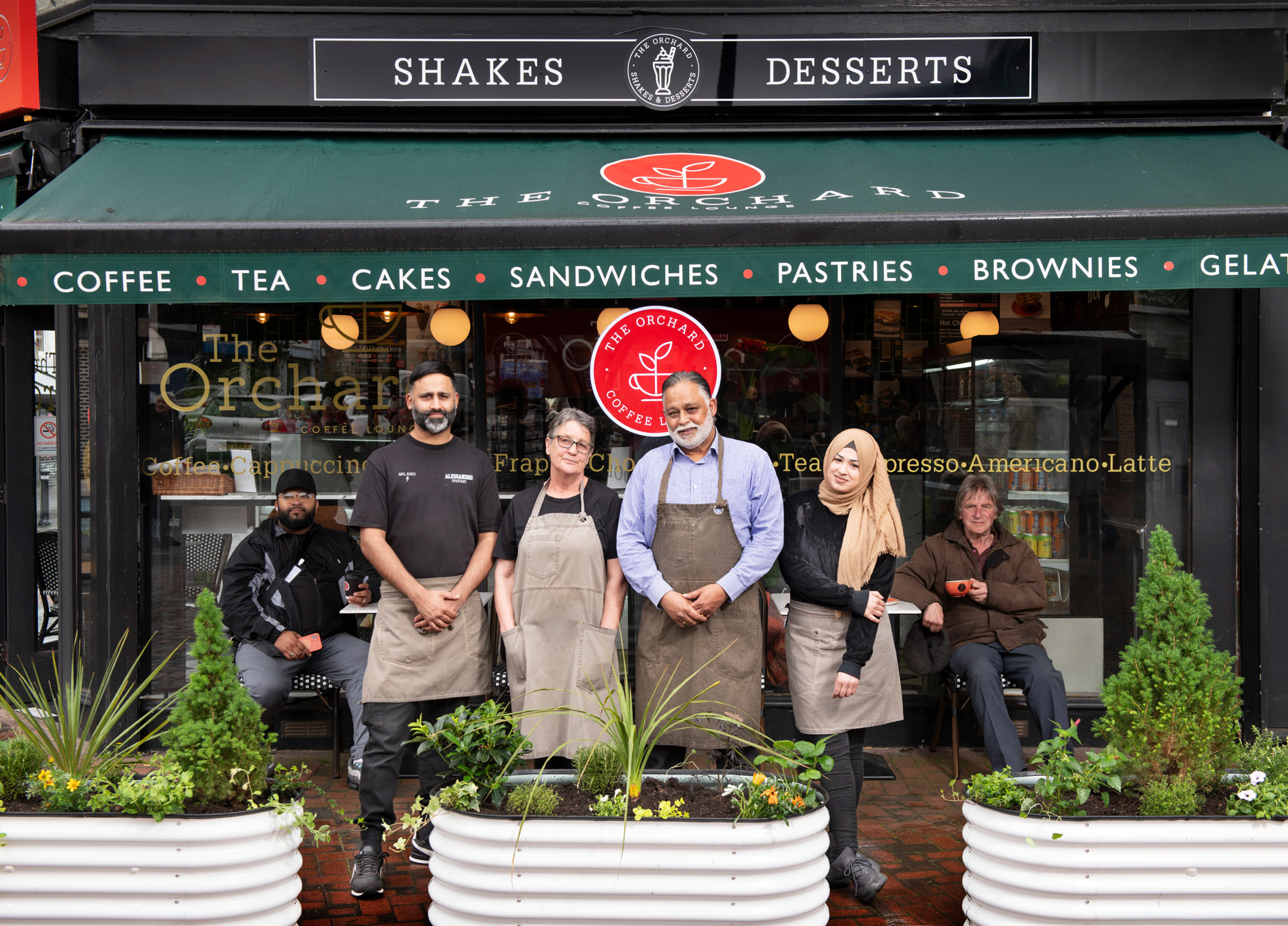 Colour photo of a posed group of coffee shop staff and customers on the street outside The Orchard coffee shop.