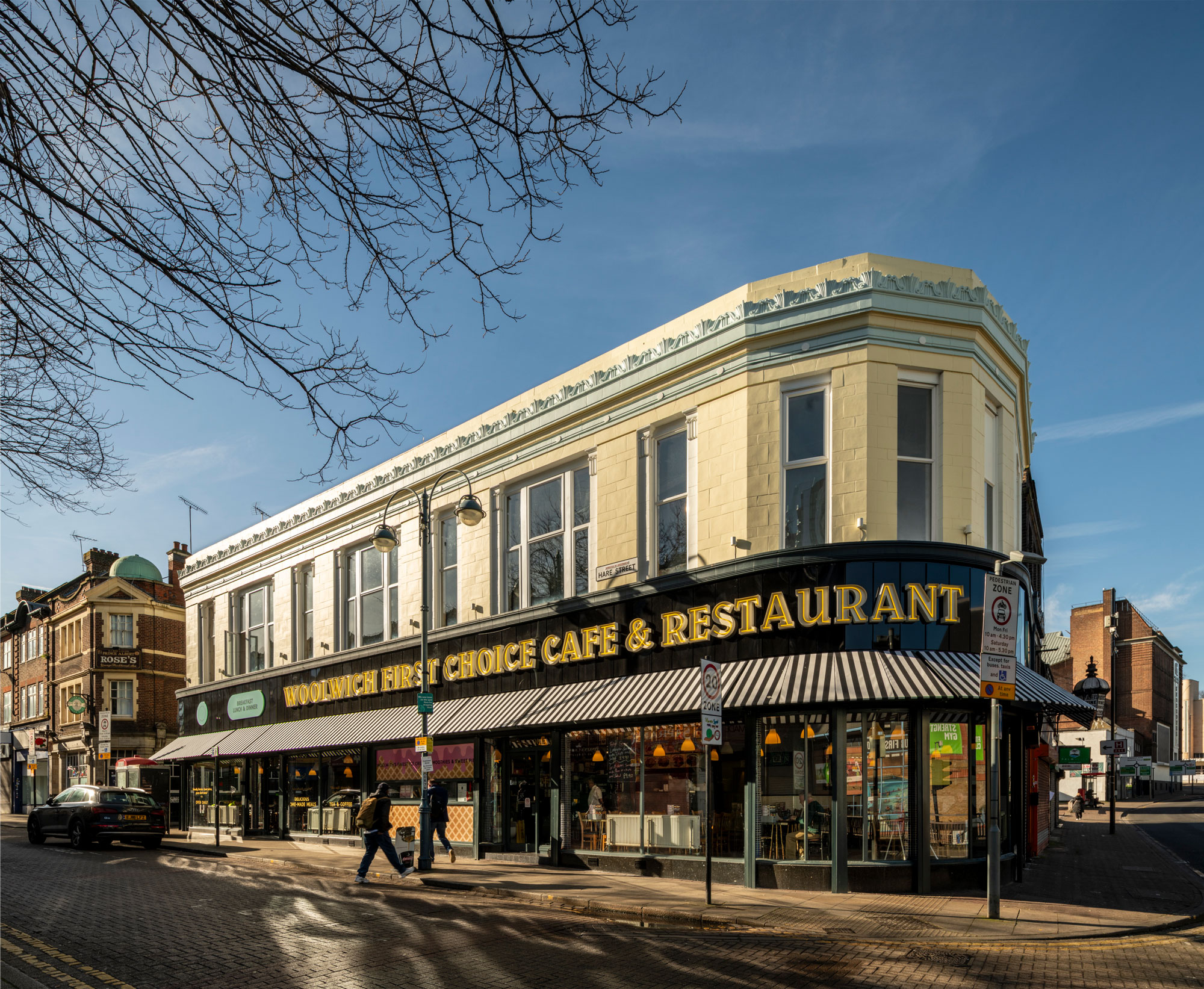 Colour photo of a corner building with restaurant on the ground floor and an upper floor with yellow tiles.
