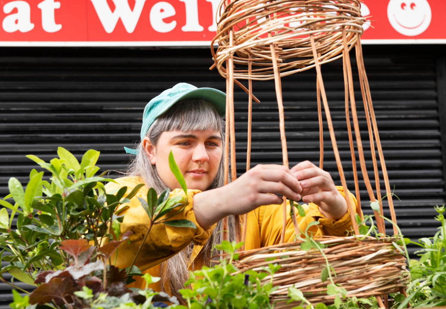 A young woman arranging a display of plants in front of a shuttered shop.