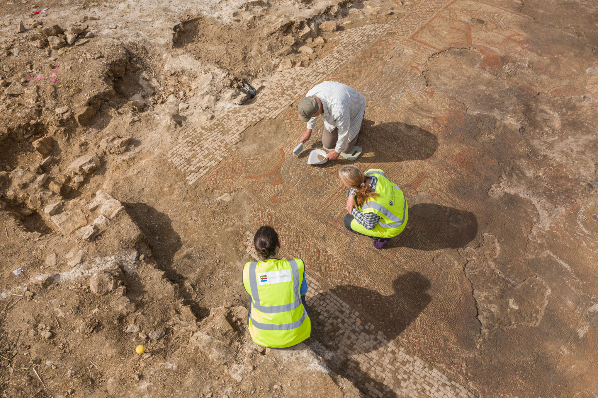 Archaeologists excavating a Roman Mosaic with human figures and a decorative border.
