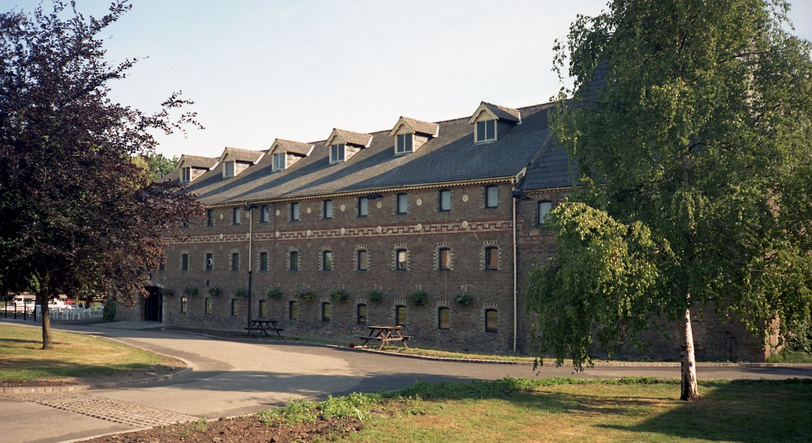 A colour photograph of the exterior of a former maltings building with a contrasting brick frieze band running above the second storey.