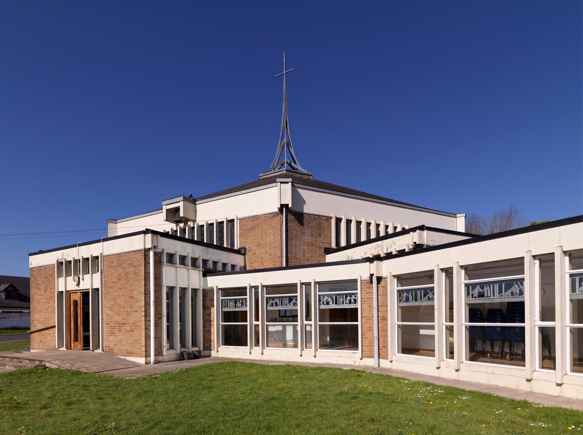 A brick built church building with large windows and a hexagonal spire.