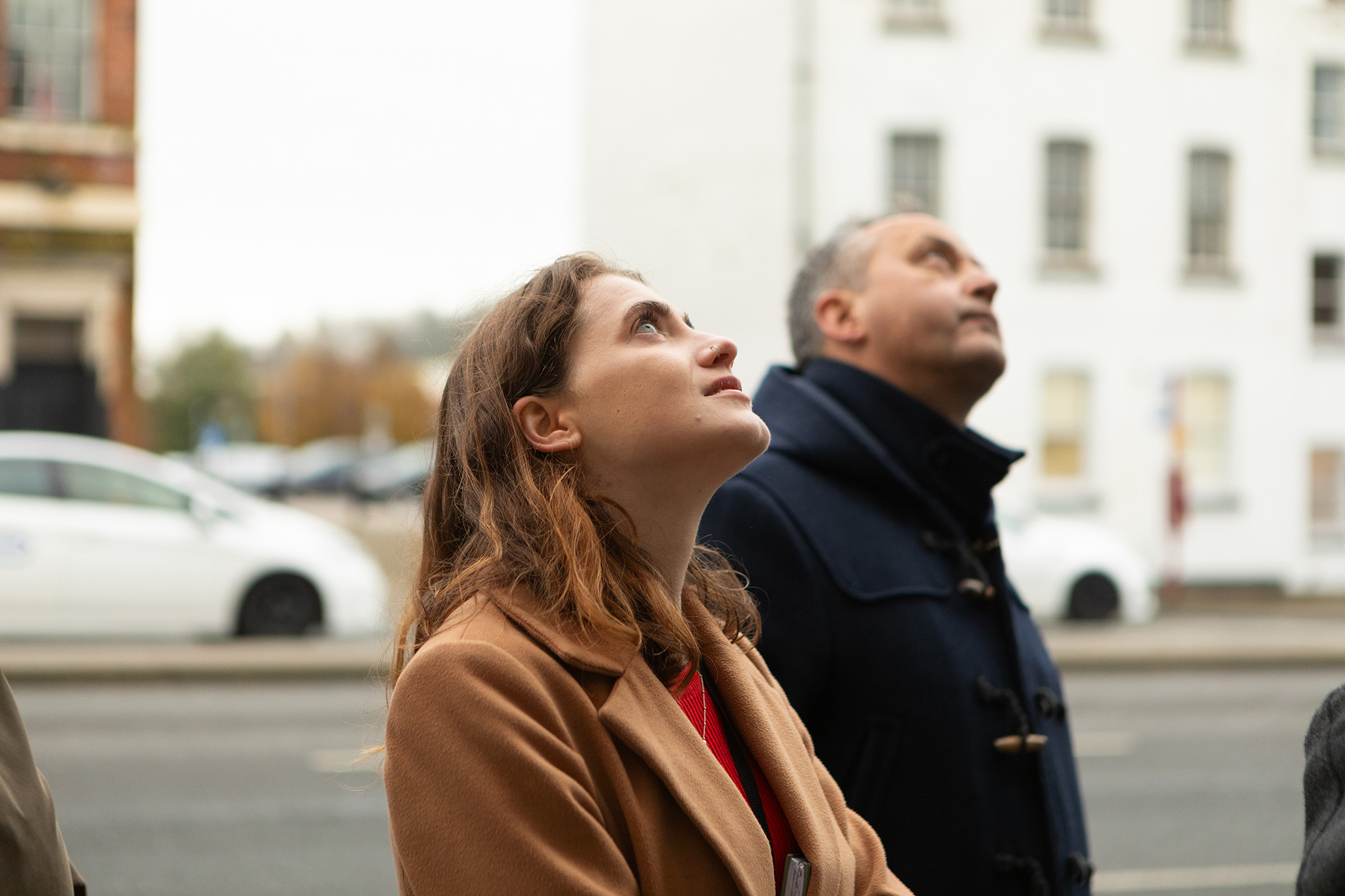 Two people, one in foreground and in focus, looking up to a subject in the street out of the frame