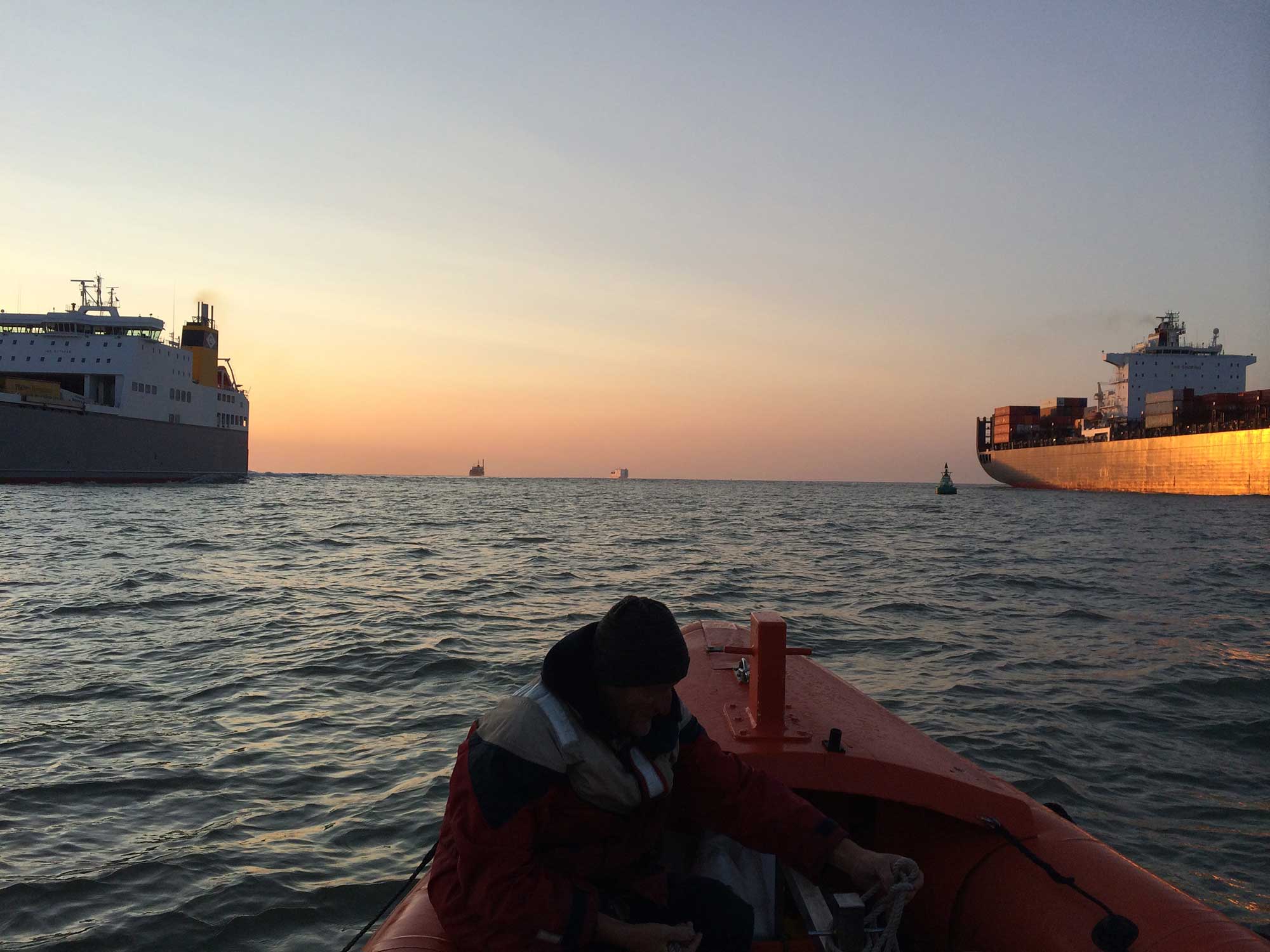 Busy shipping lane with large container ships in the background and surrounding a small boat.