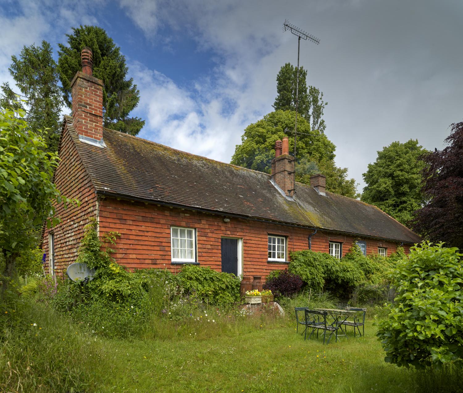 A single storey building with red tile hung walls. Garden to the front and vegetation surrounding the lower walls.