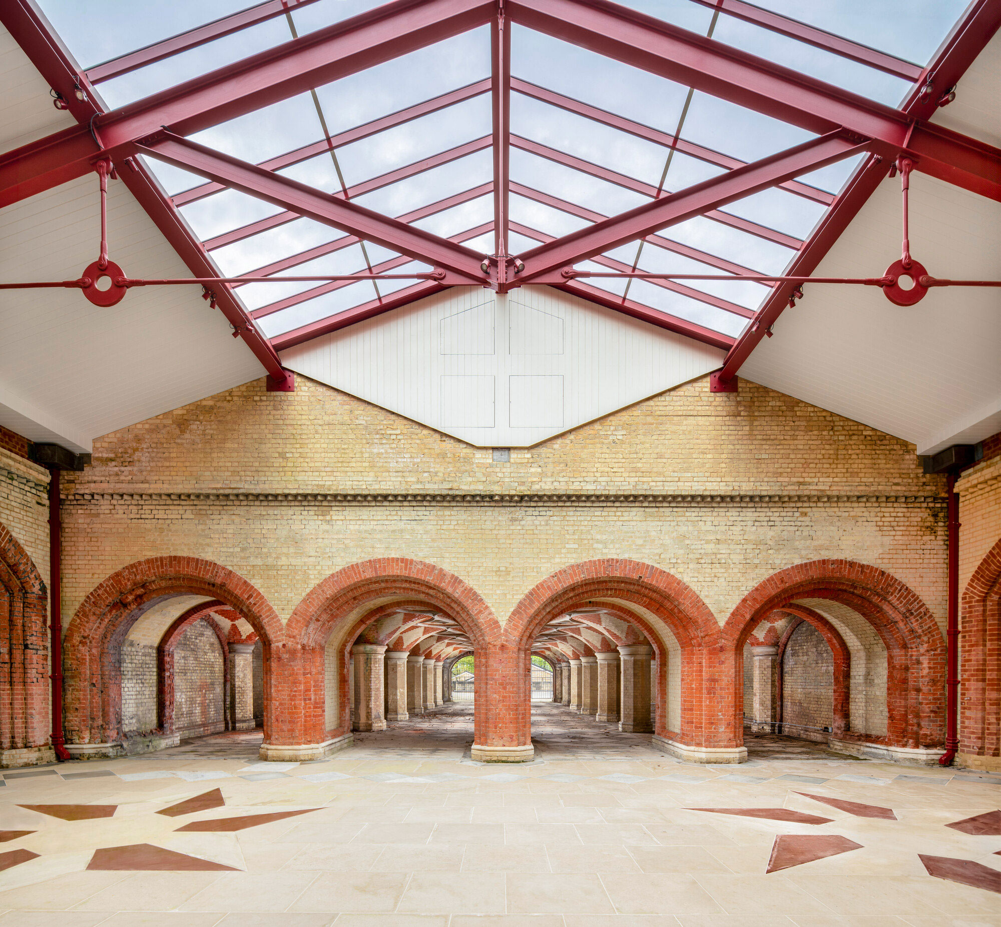 Colour photo showing a spacious interior with a glass roof, brick arches and a patterned floor, blending historic and modern architectural elements.