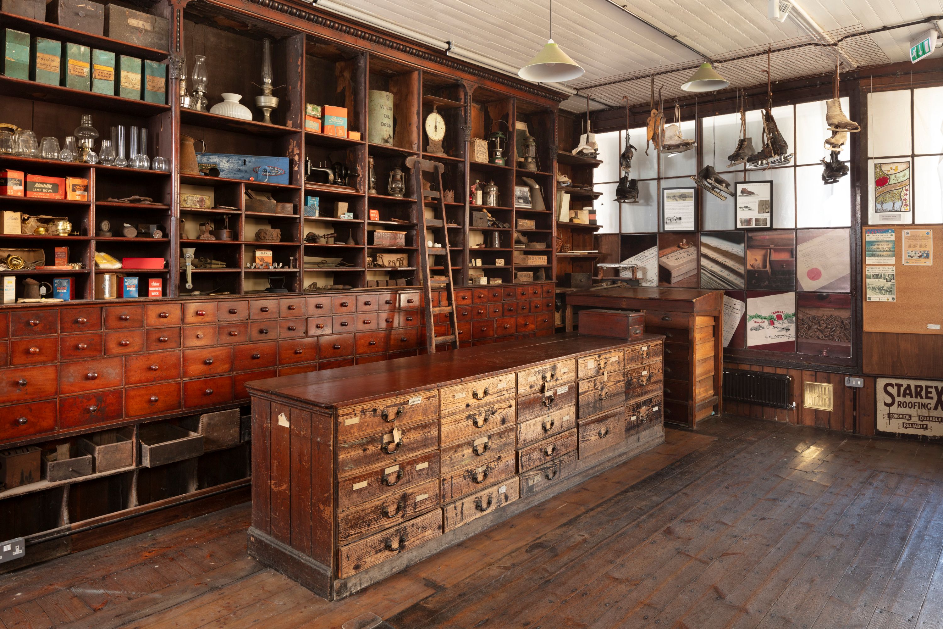 A colour photograph of the interior of The former J H Adams and Sons building, now Adams Heritage Centre. The interior shows the shop counter and wooden shelving.