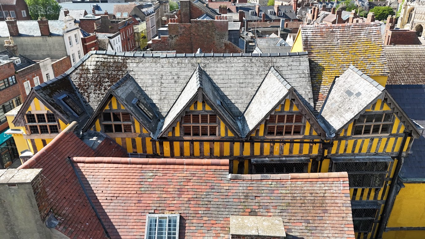 A rooftop view of 26 Westgate, Gloucester, shows the tiled roof and timbered frontage with vibrant yellow paint