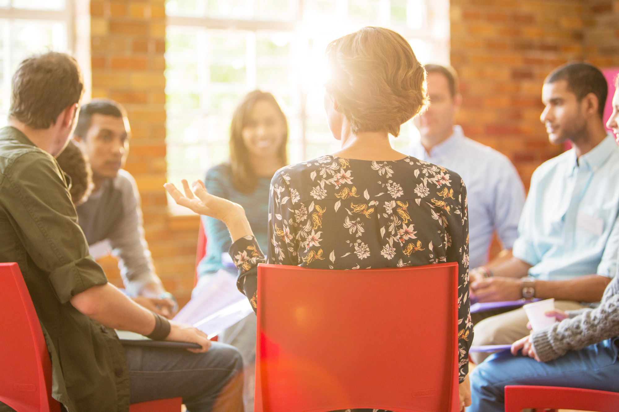 A woman is talking to a small group of people seated in a circle.