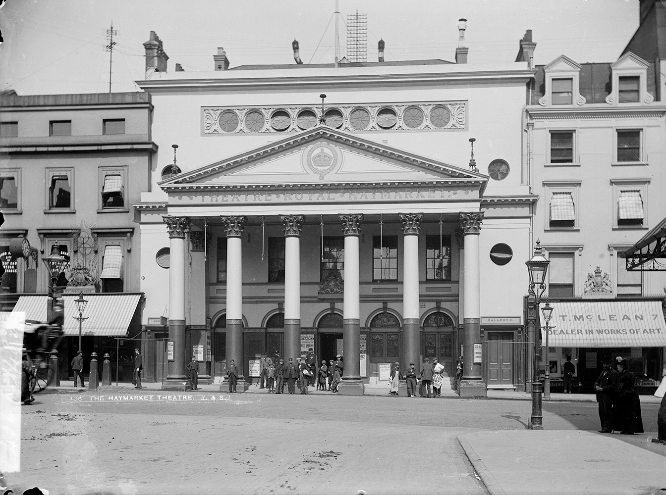 A black-and-white photo of a four-storey urban neoclassical theatre with a portico supported by six classically proportioned columns. Text on the pediment reads "Theatre Royal Haymarket". 