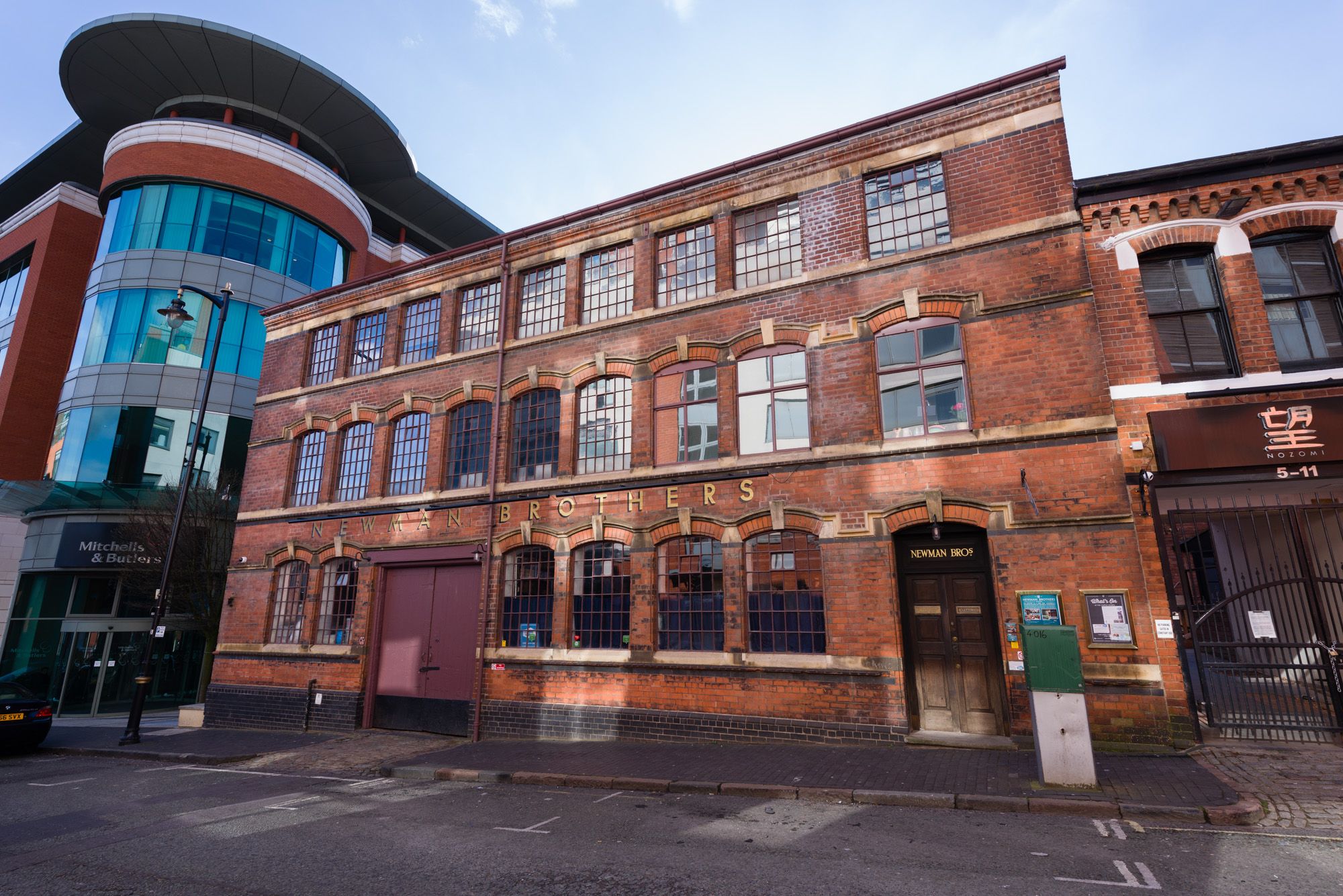 Landscape photograph of the front exterior of the Coffin Works, which is a three story red brick Victorian building with 'Newman Brothers' in gold lettering just above the ground floor