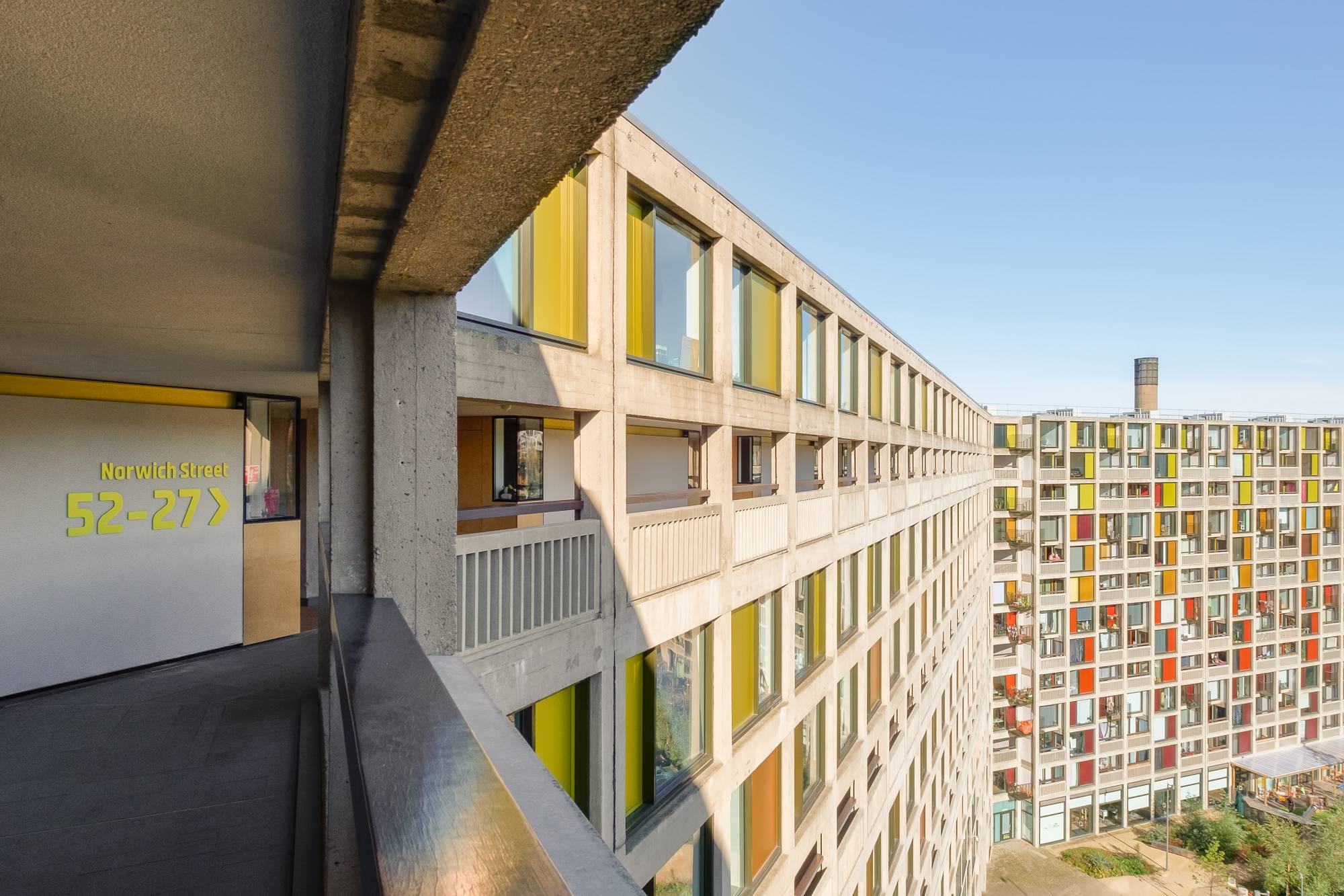 Phase 1 of Park Hill showing ‘streets in the sky’ corridor and external view of refurbished building façade. The facade displays the original concrete framing and bold coloured panels next to the windows.  