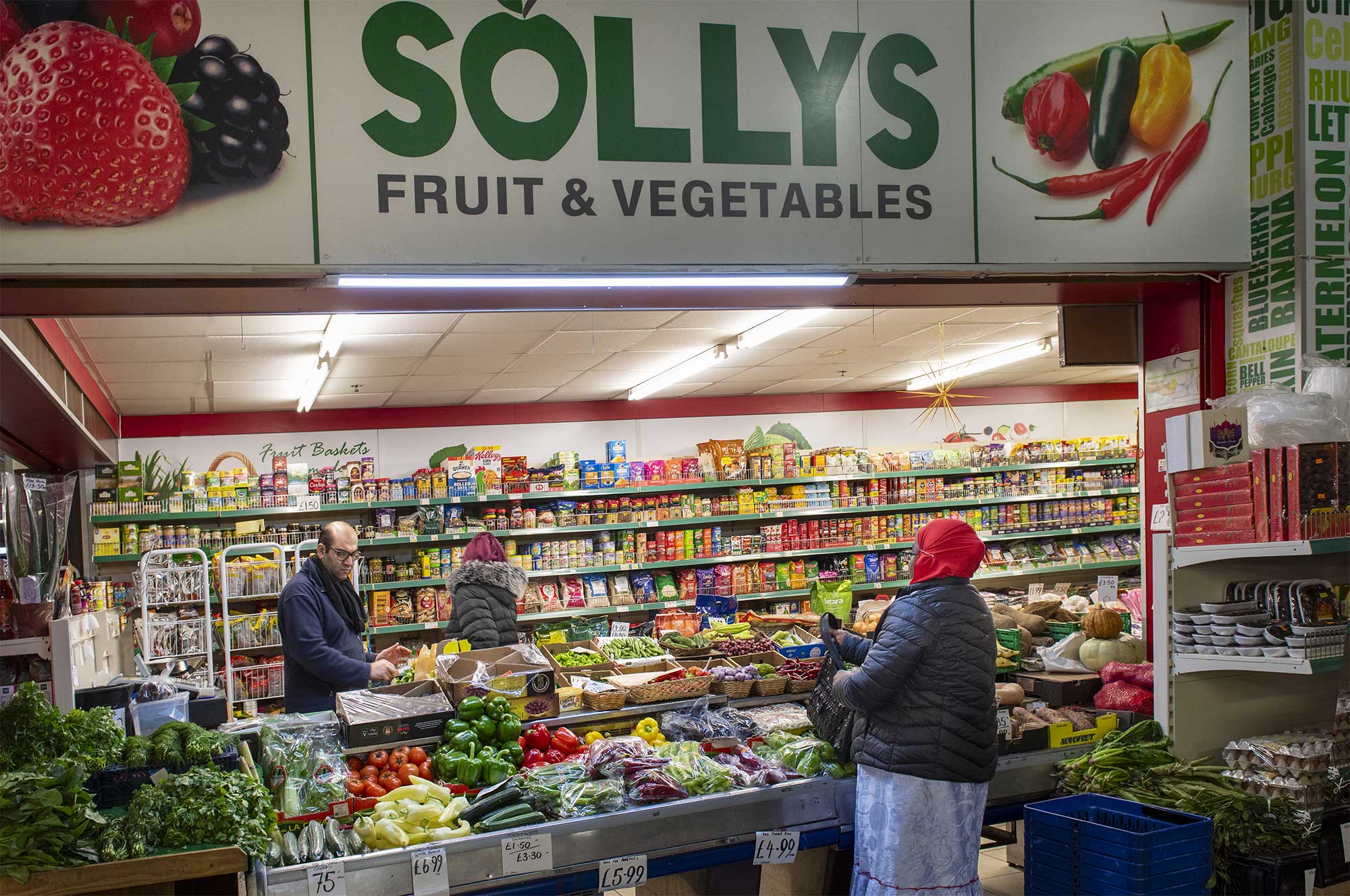 Two individual's shopping for fruit and vegetables at a brightly coloured market stall. 