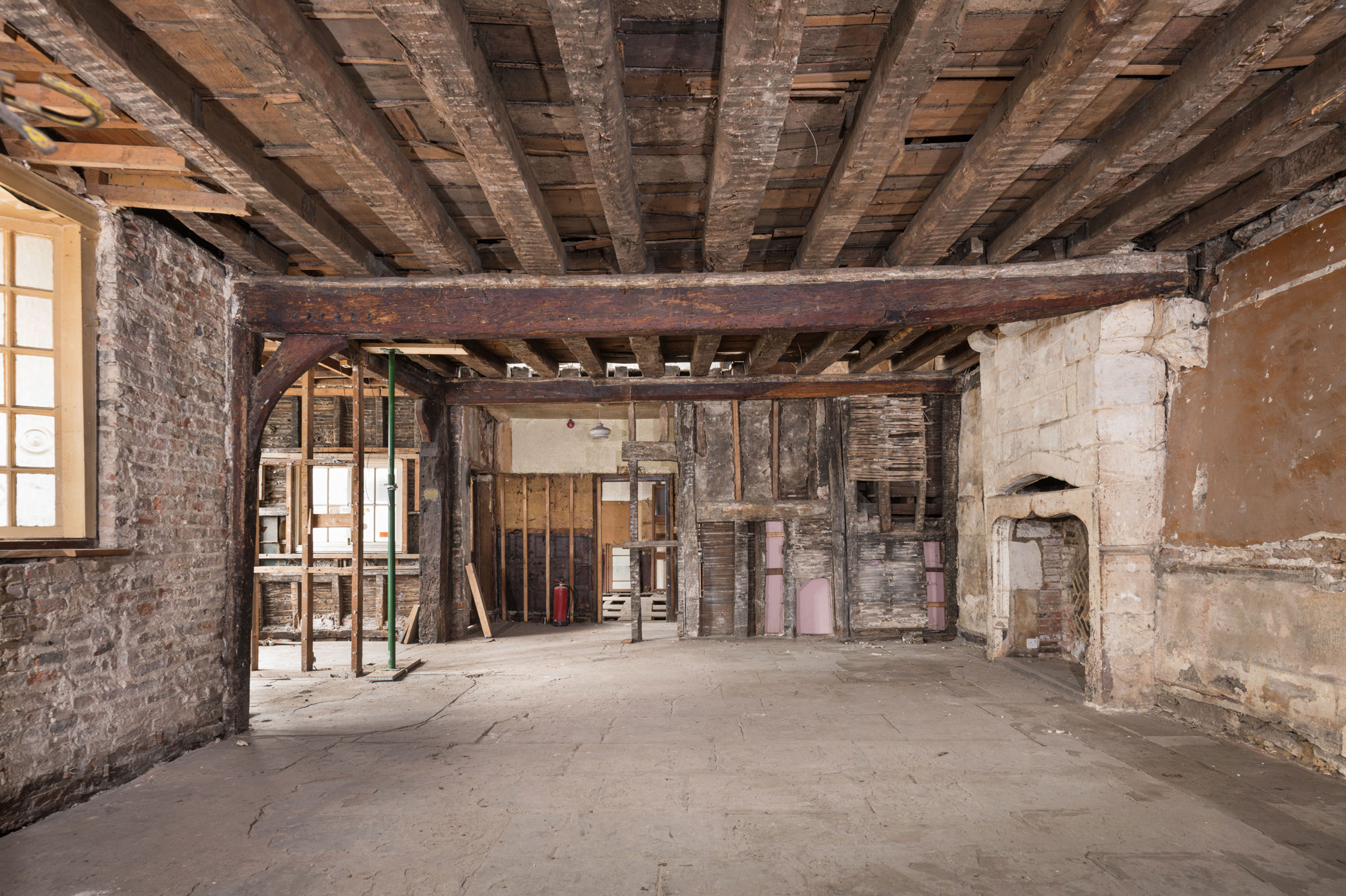 Interior view of rooms showing details of ceiling beams and a timber dividing wall, with a stone fireplace to the right.