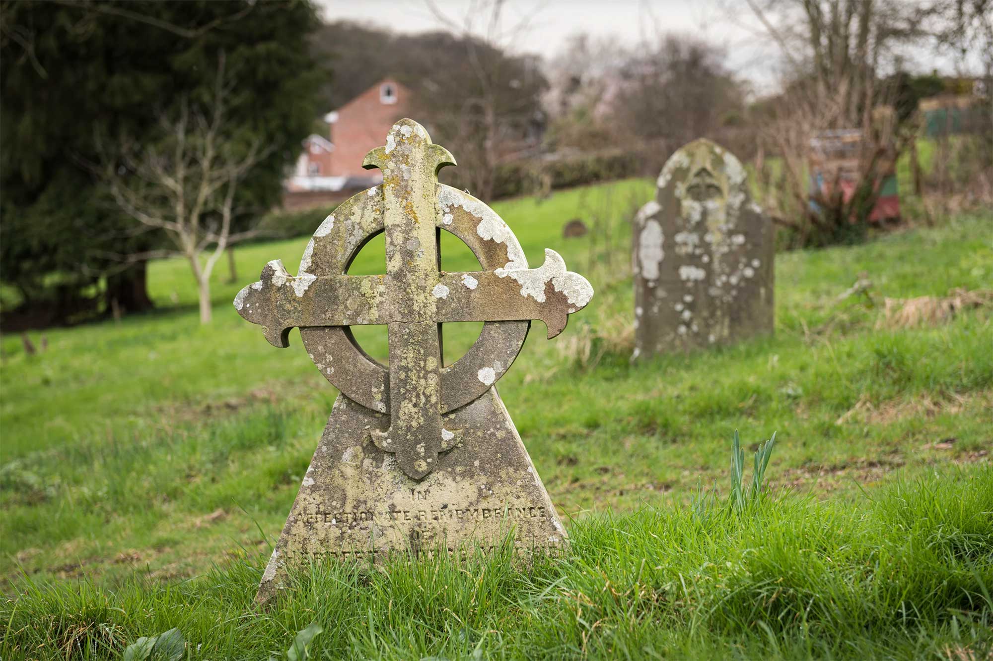 A photograph of a graveyard with a round-headed cross headstone in the foreground. 