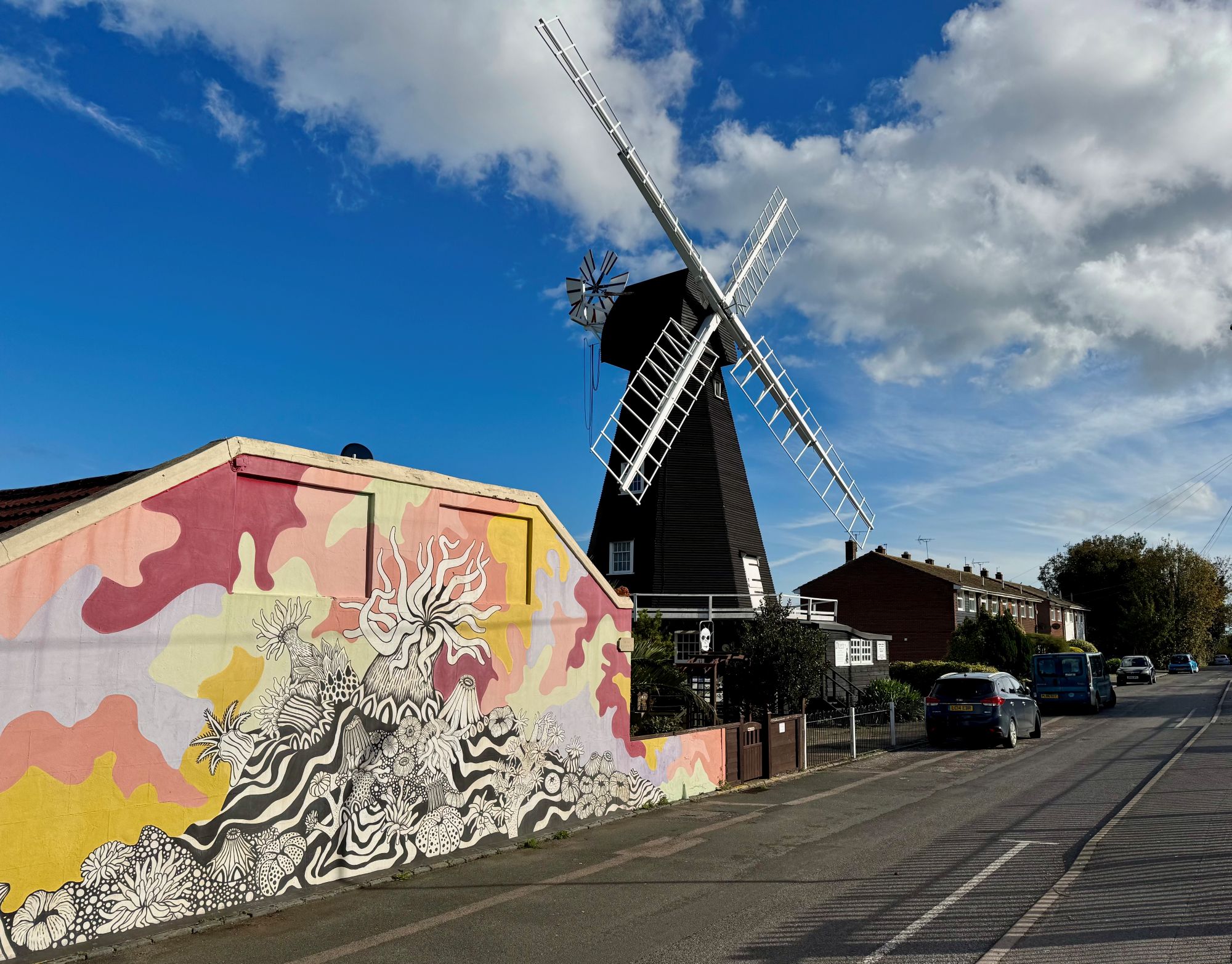 A photo of a windmill against a blue sky near a wall with a colourful mural