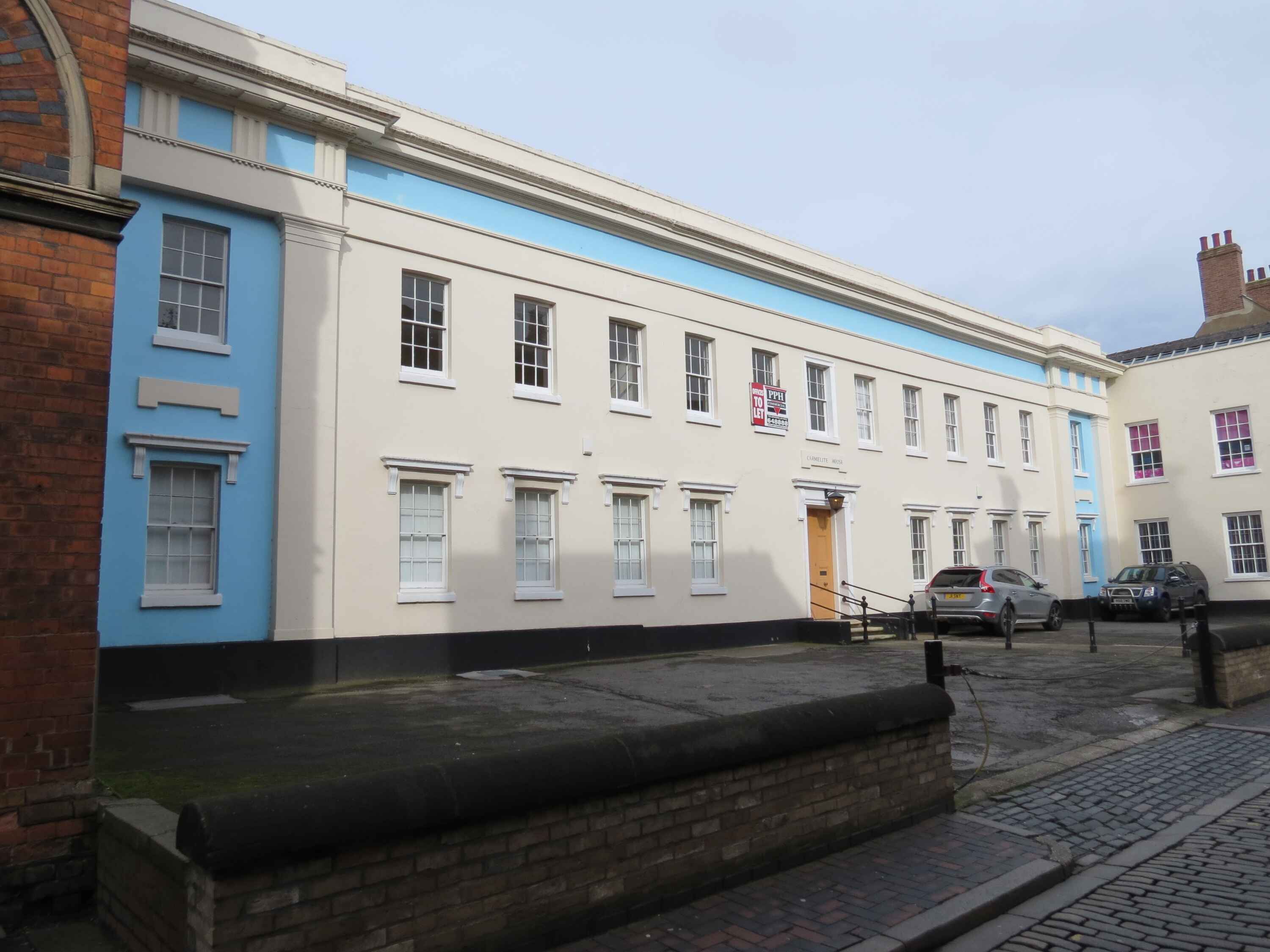 Front of Carmelite House painted white and blue with a couple of cars parked outside.