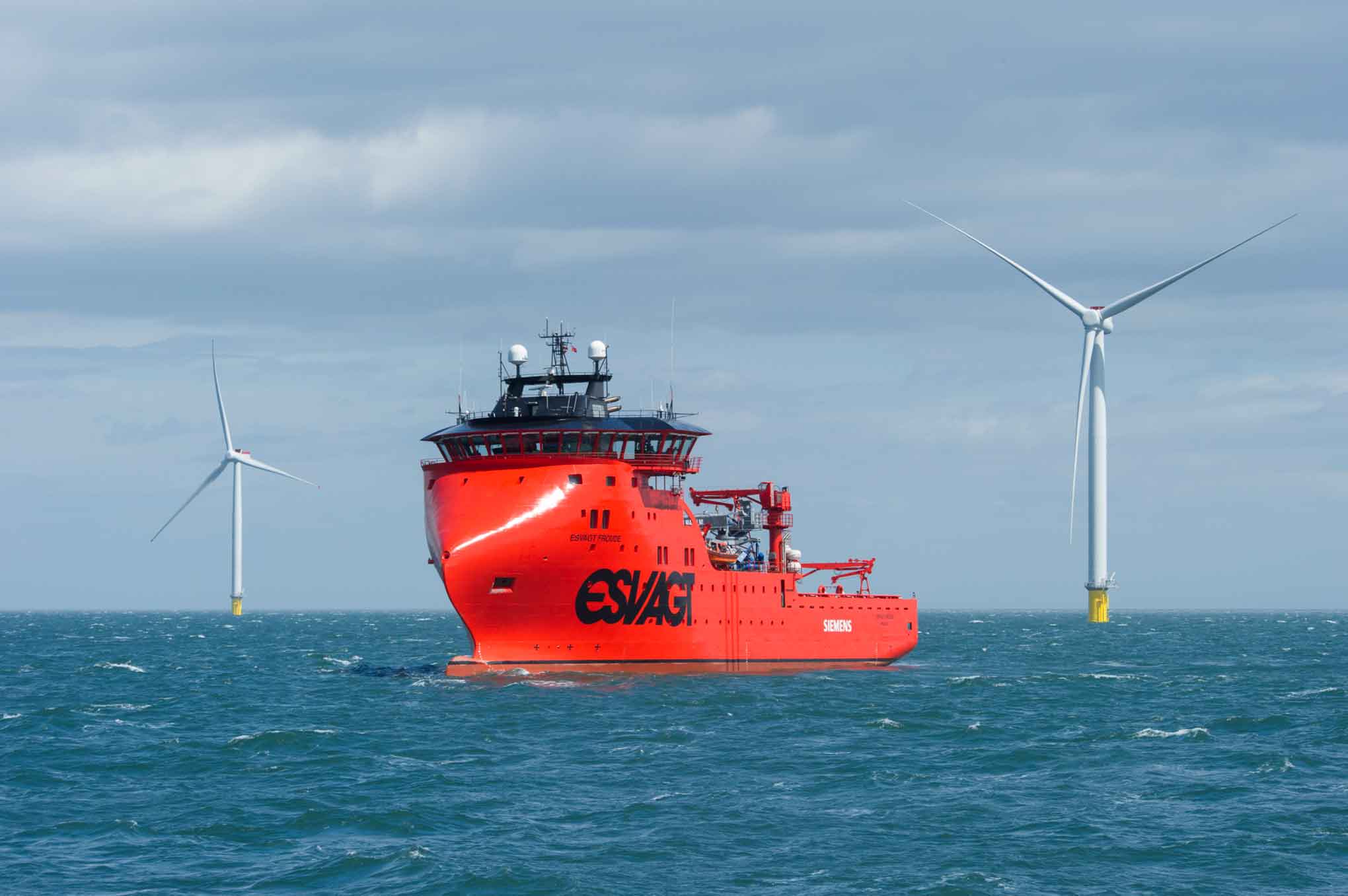 A ship with two large wind turbines in the background