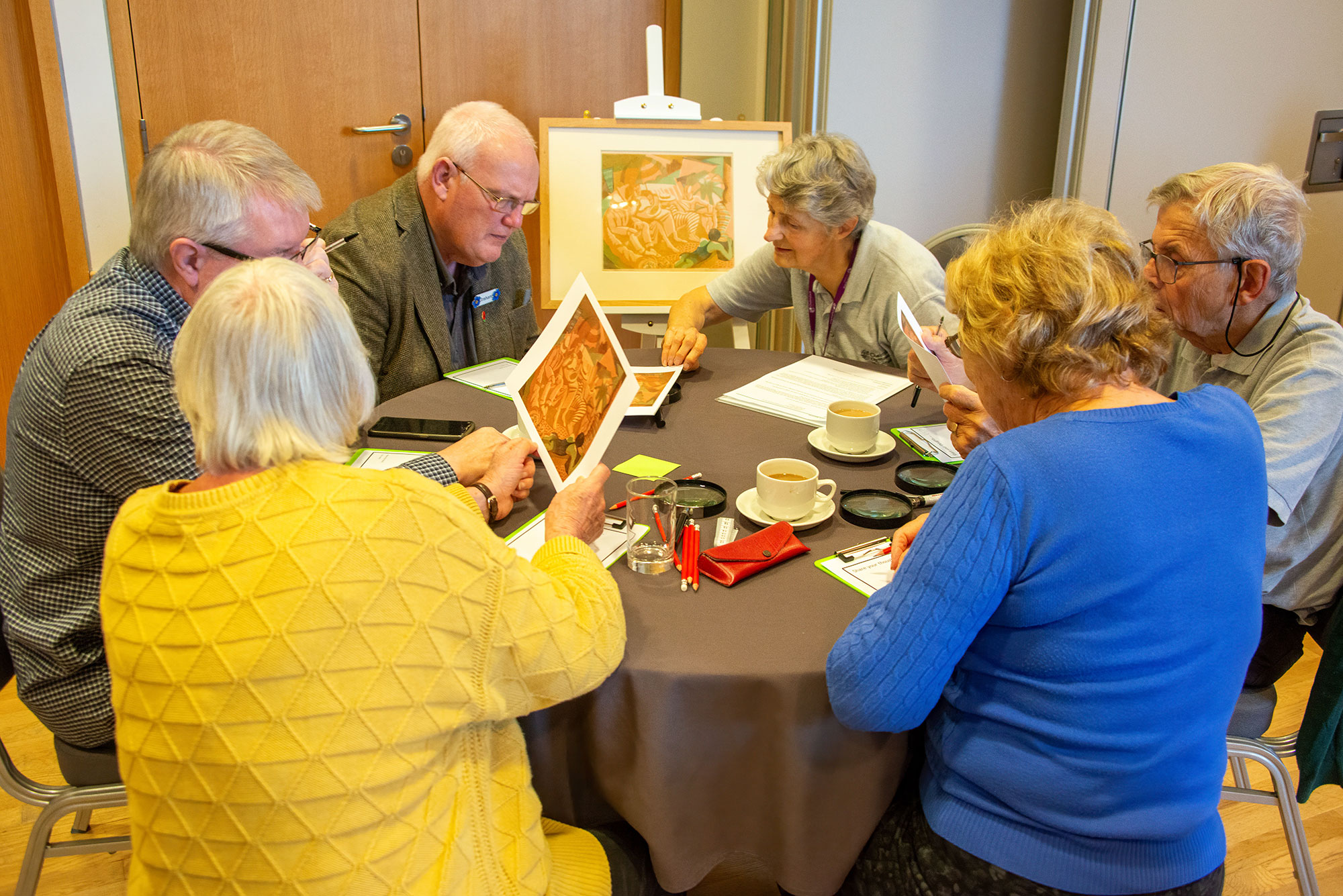 A group of people sitting around a table looking at prints of artwork.
