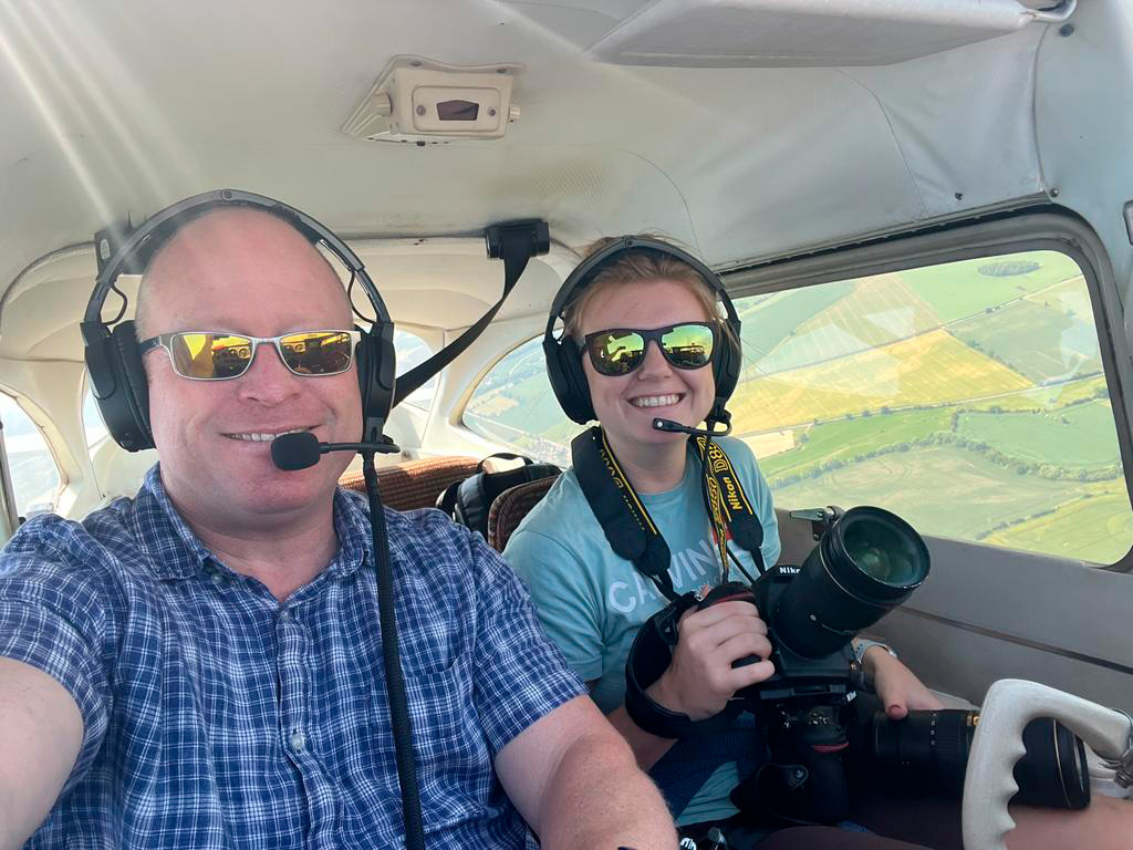 A pilot and photographer during a flight in a light aircraft; through the windows a patchwork landscape of fields is visible.