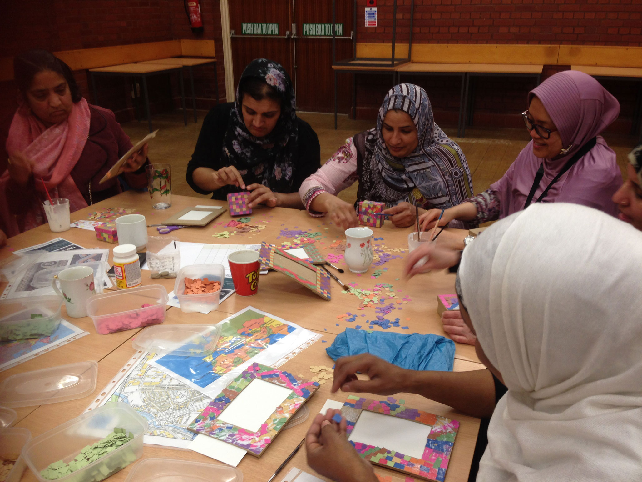 A group of women of south-east Asian heritage sat around a table taking parts in crafts.