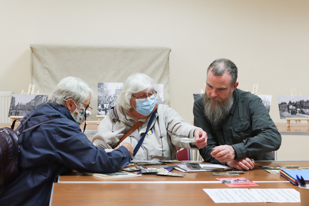 Photo of 2 women wearing face masks seated at a table looking at old photos with photographer Tony Mallon.