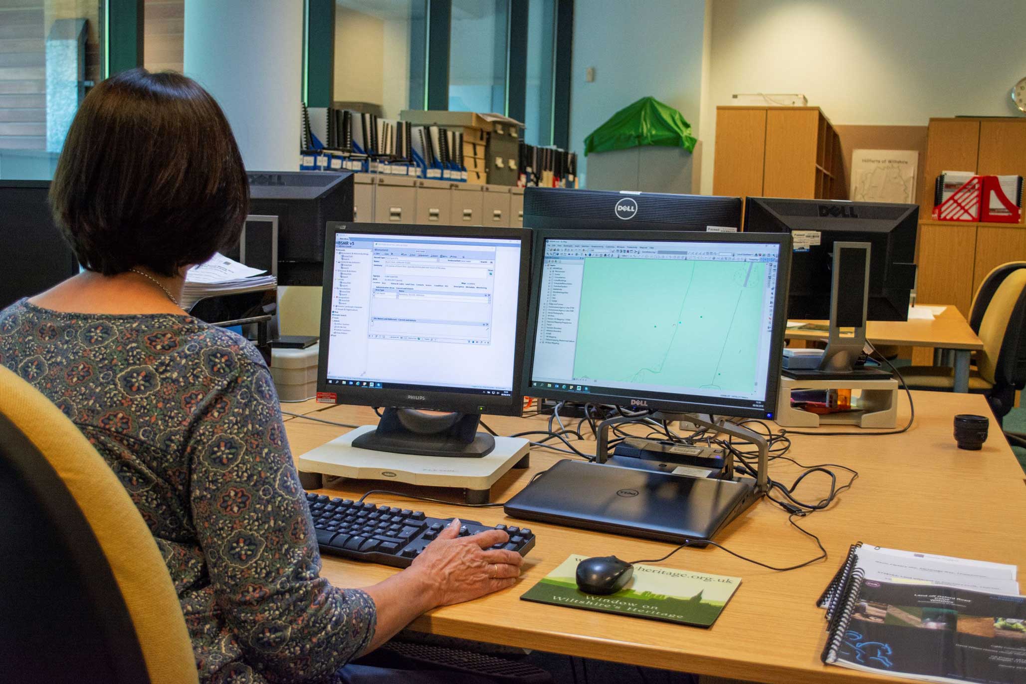 A woman working on a computer with two screens in front of her.