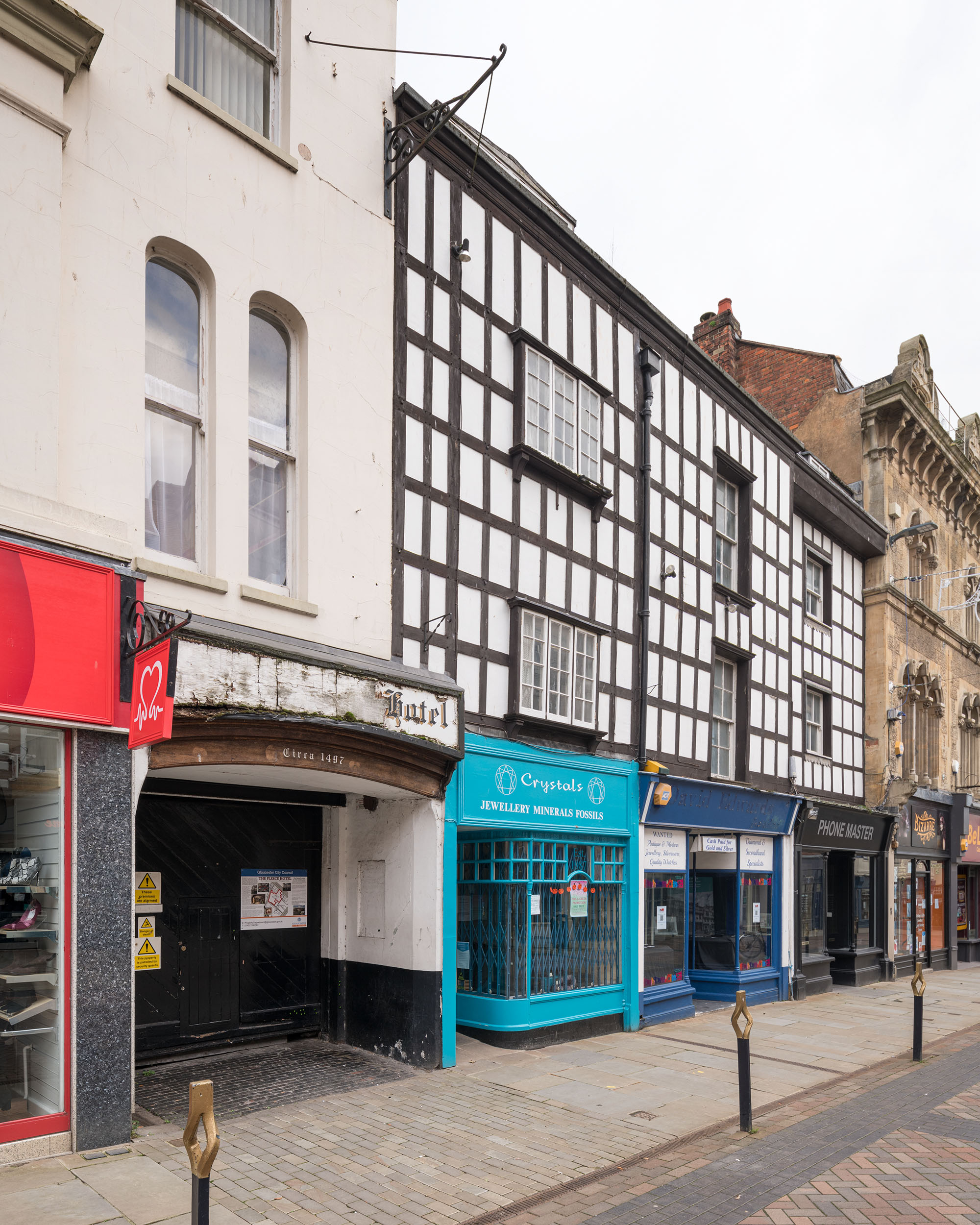 An image of the front of a historic building on a high street. The building needs repair. Its first floor is timber framed. There is an archway entrance over which is written 'circa 1497'.