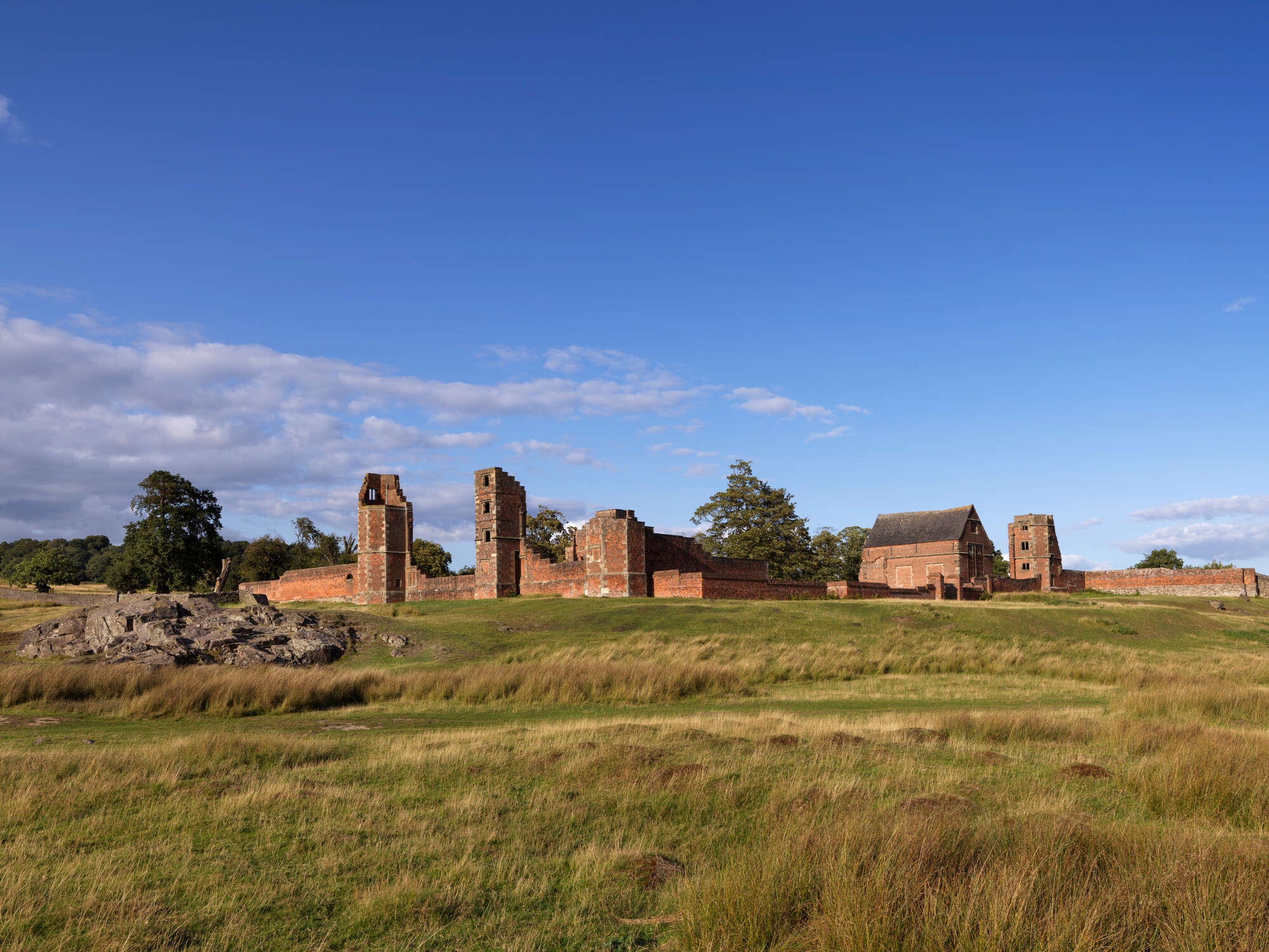 A photograph of a deer park with the ruins of a grand house in the distance.