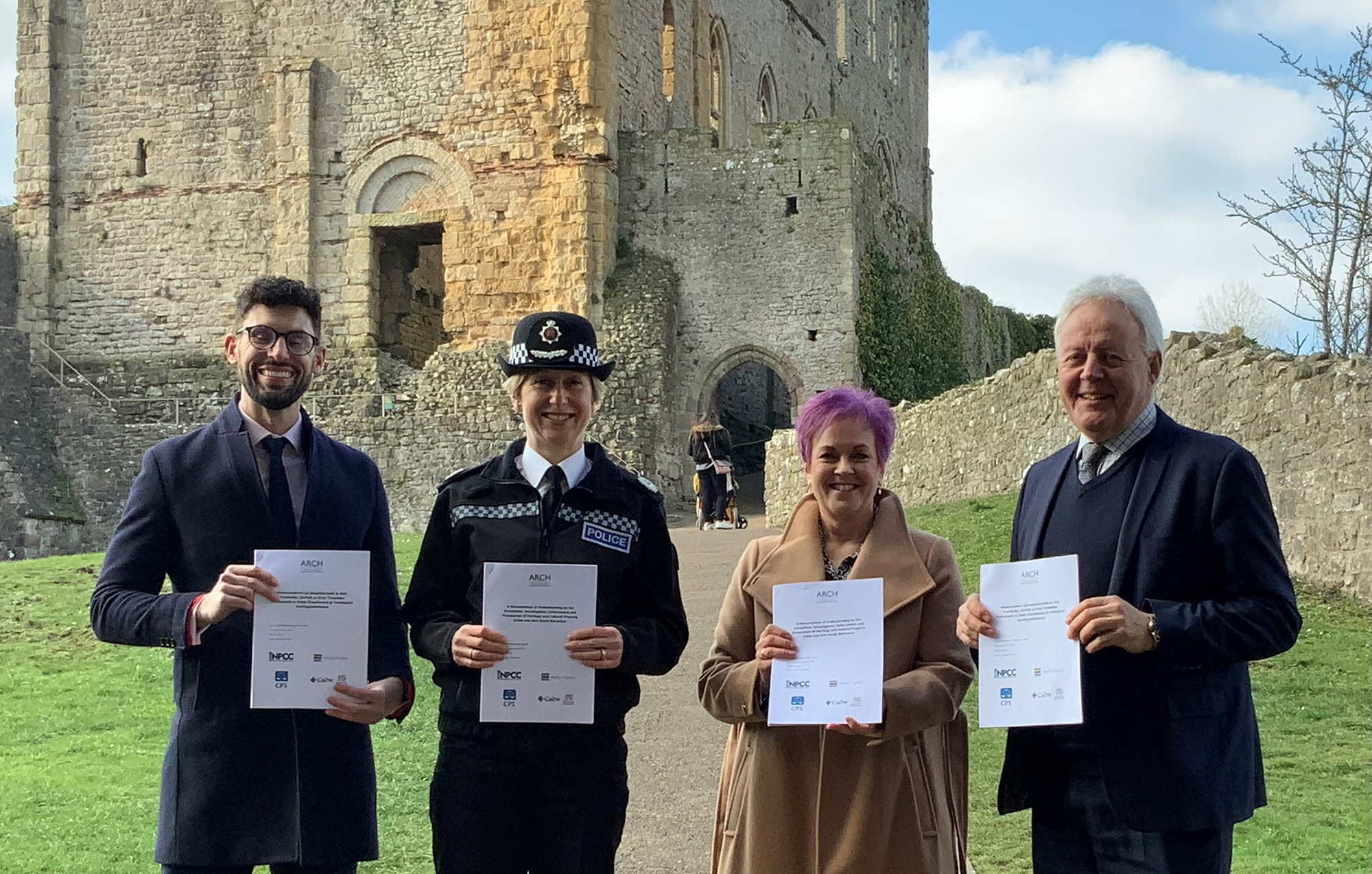 Four people each holding a document in front of castle ruins