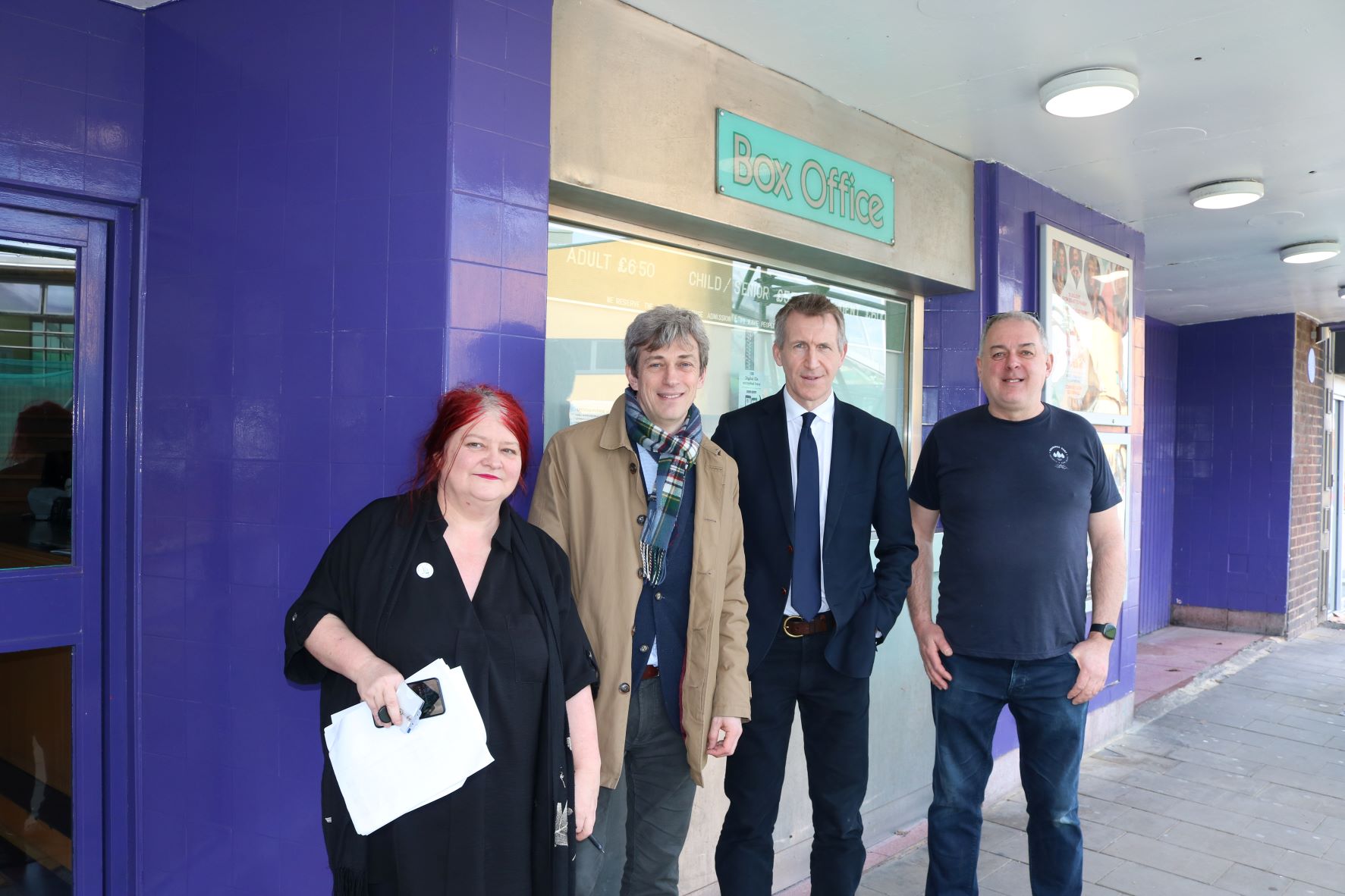 One woman and three men standing outside a building looking at the camera.