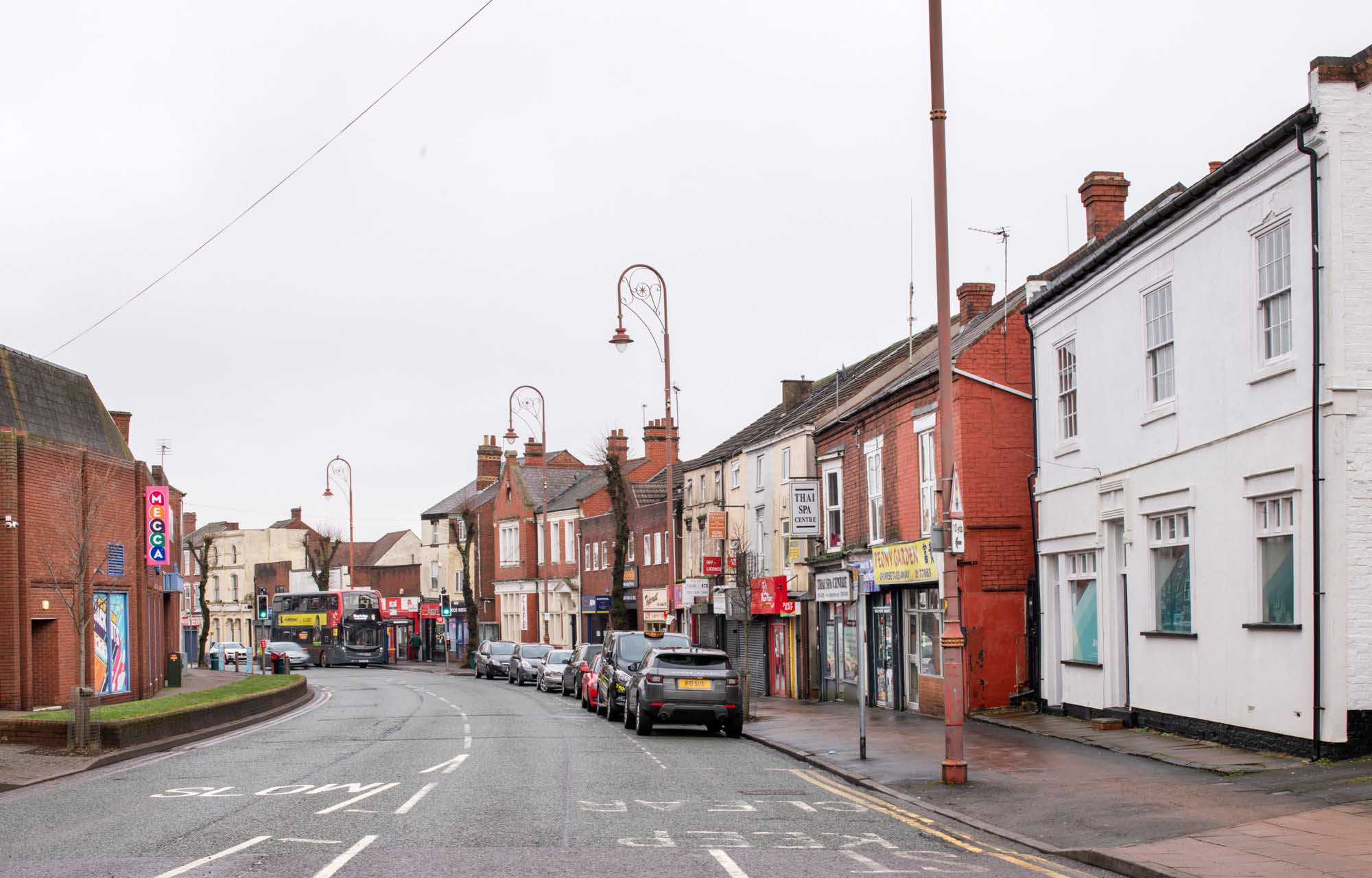 Colour photo of a quiet high street with cars parked.