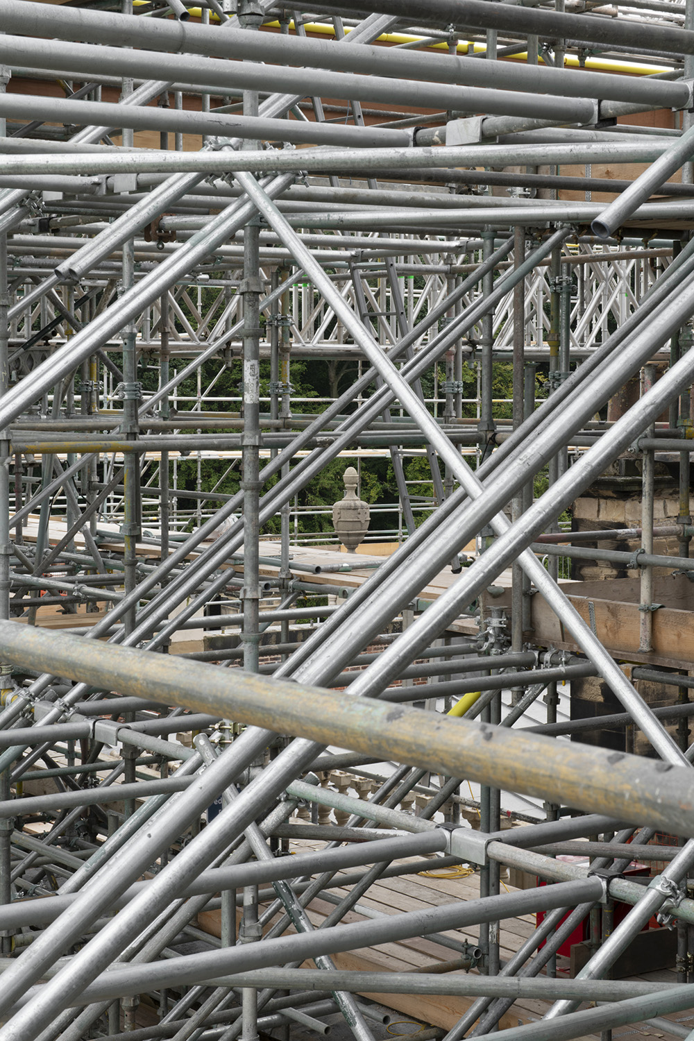 A dense grid of scaffolding with a decorative urn visible in the distance.