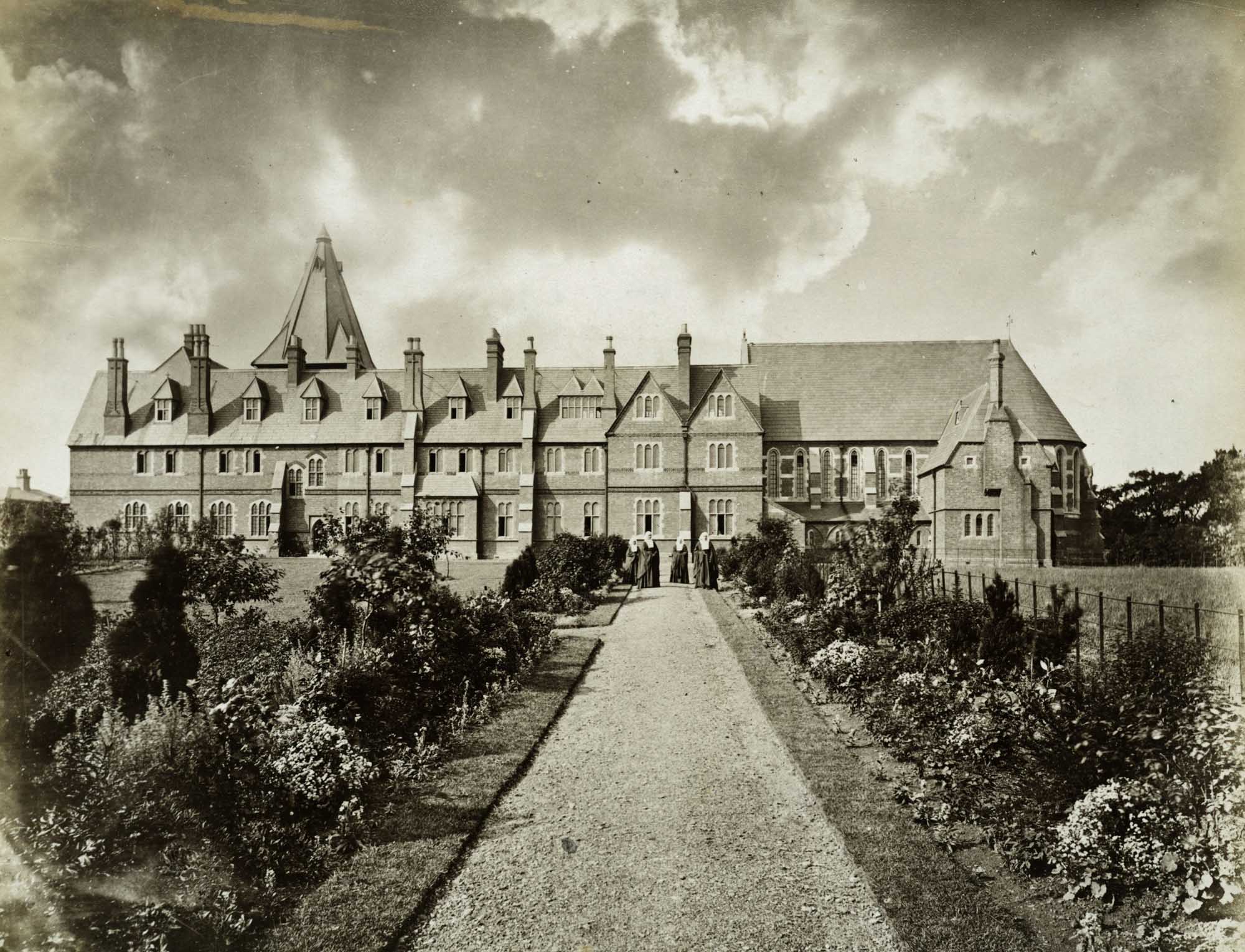 Looking along a gravel path towards the south range of the St Peter's Convent, with four nuns standing in the distance. 