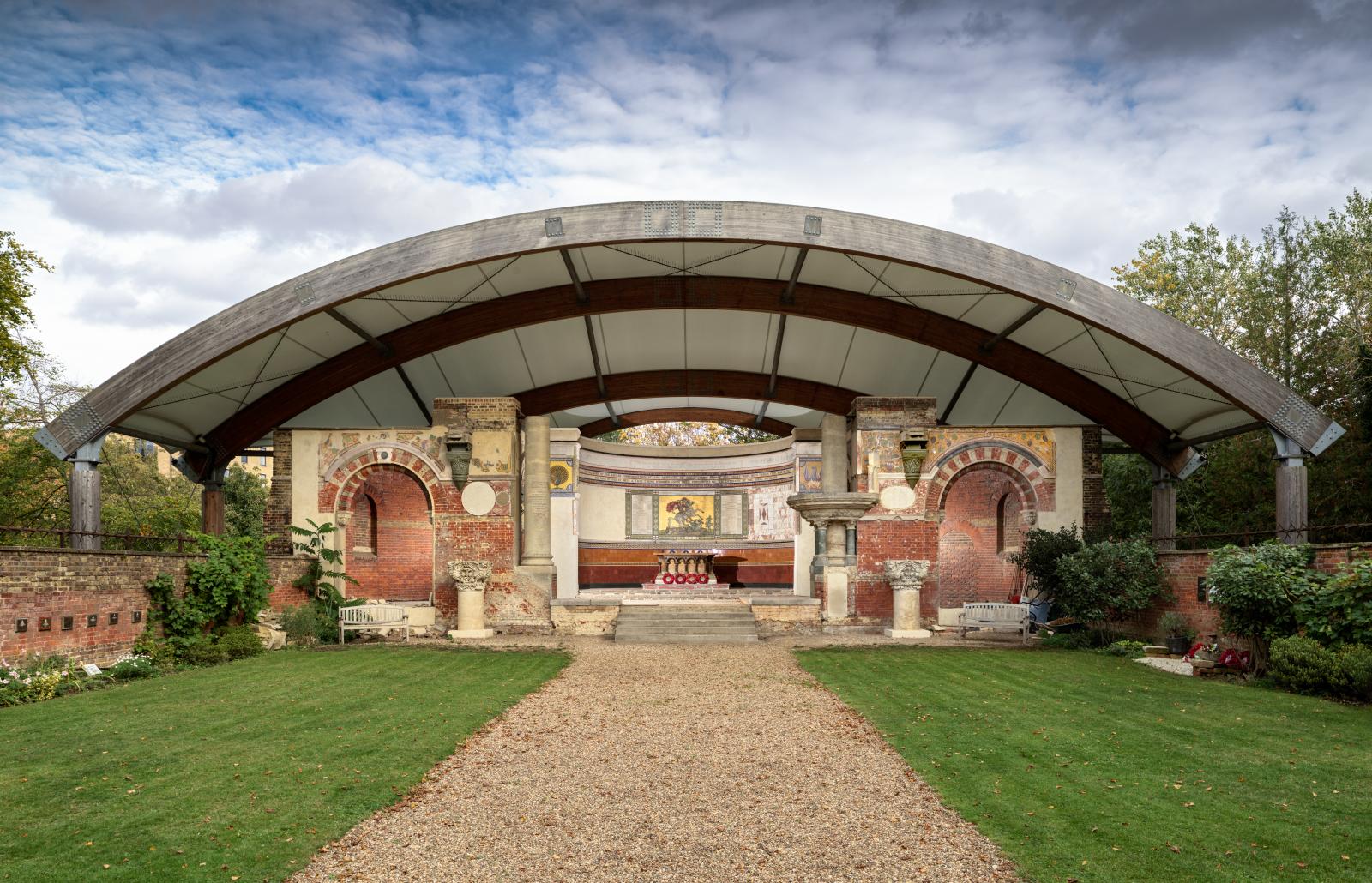 The altar, apse and end wall of a ruined church, all covered by a solid modern arched canopy
