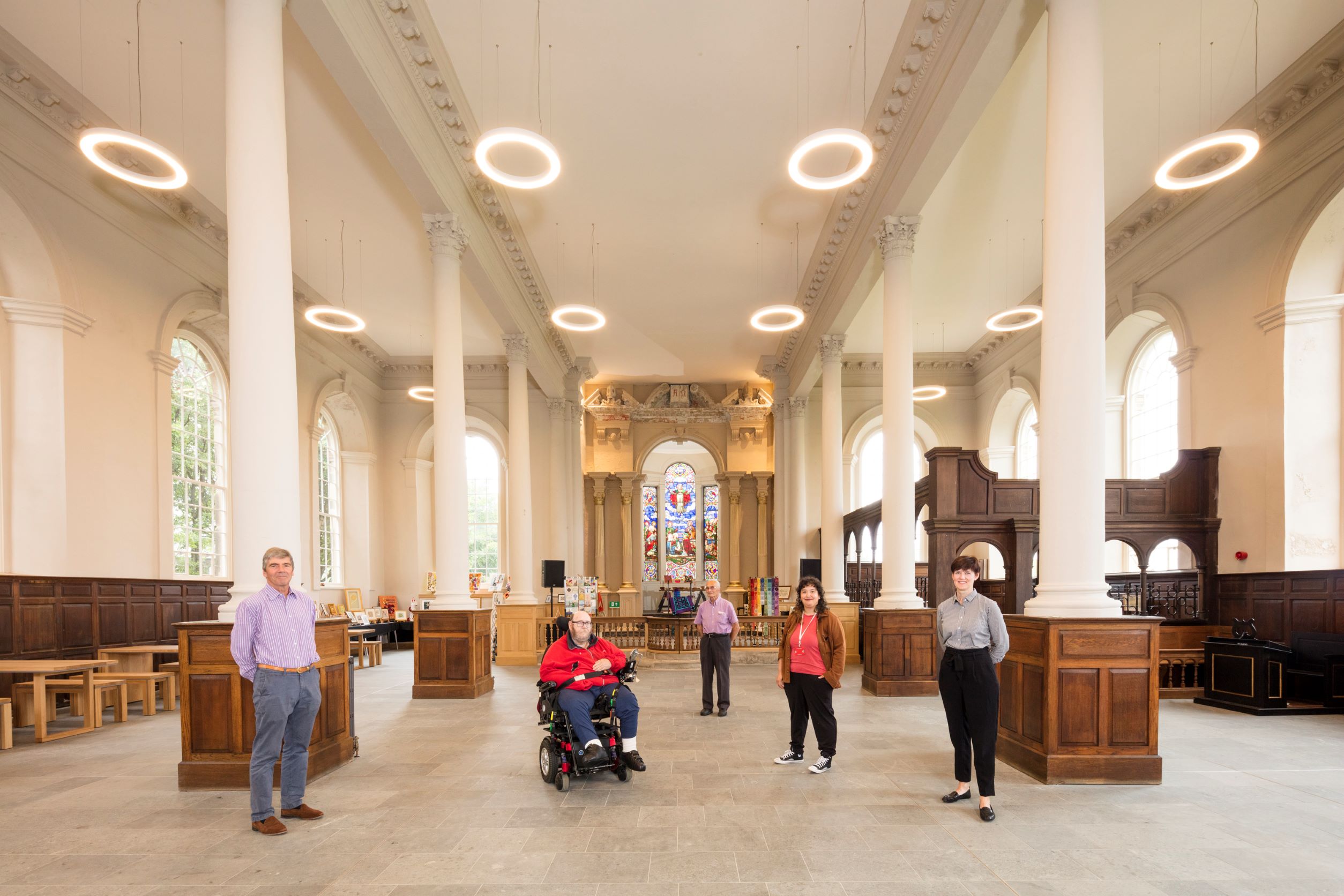 Five people standing looking at the camera inside a church. There are three men and two women. 