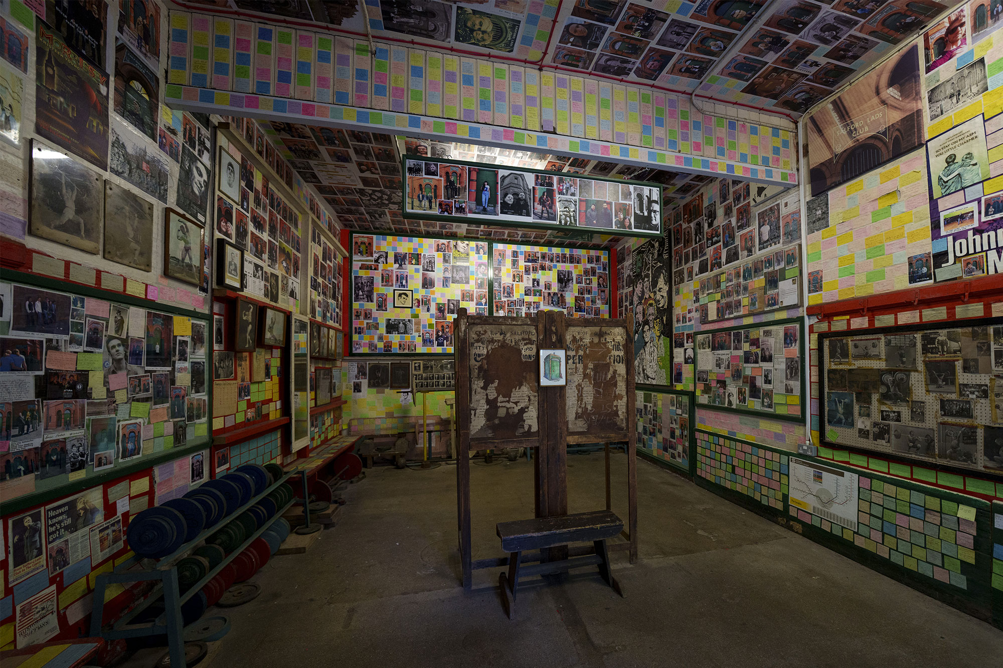 A room covered in photographs and colourful post-it notes left by fans of The Smiths who have visited Salford Lads and Girls Club.  The building is internationally recognised through its association with The Smiths, following an iconic photograph taken outside its front entrance which became the inside cover of their 1985 album The Queen is Dead. 