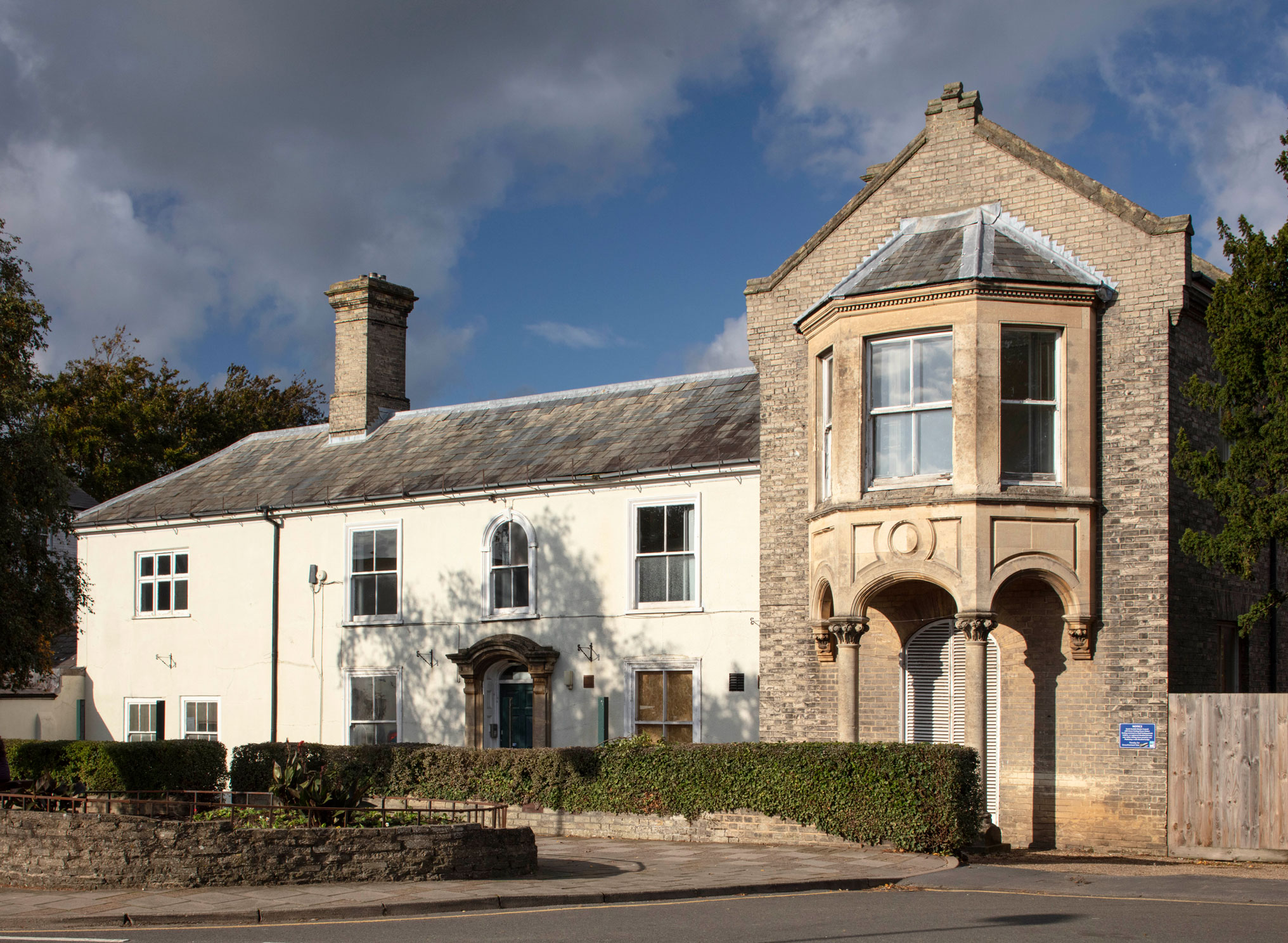 View of a two storey rendered Georgian building with a taller, later Victorian brick wing.