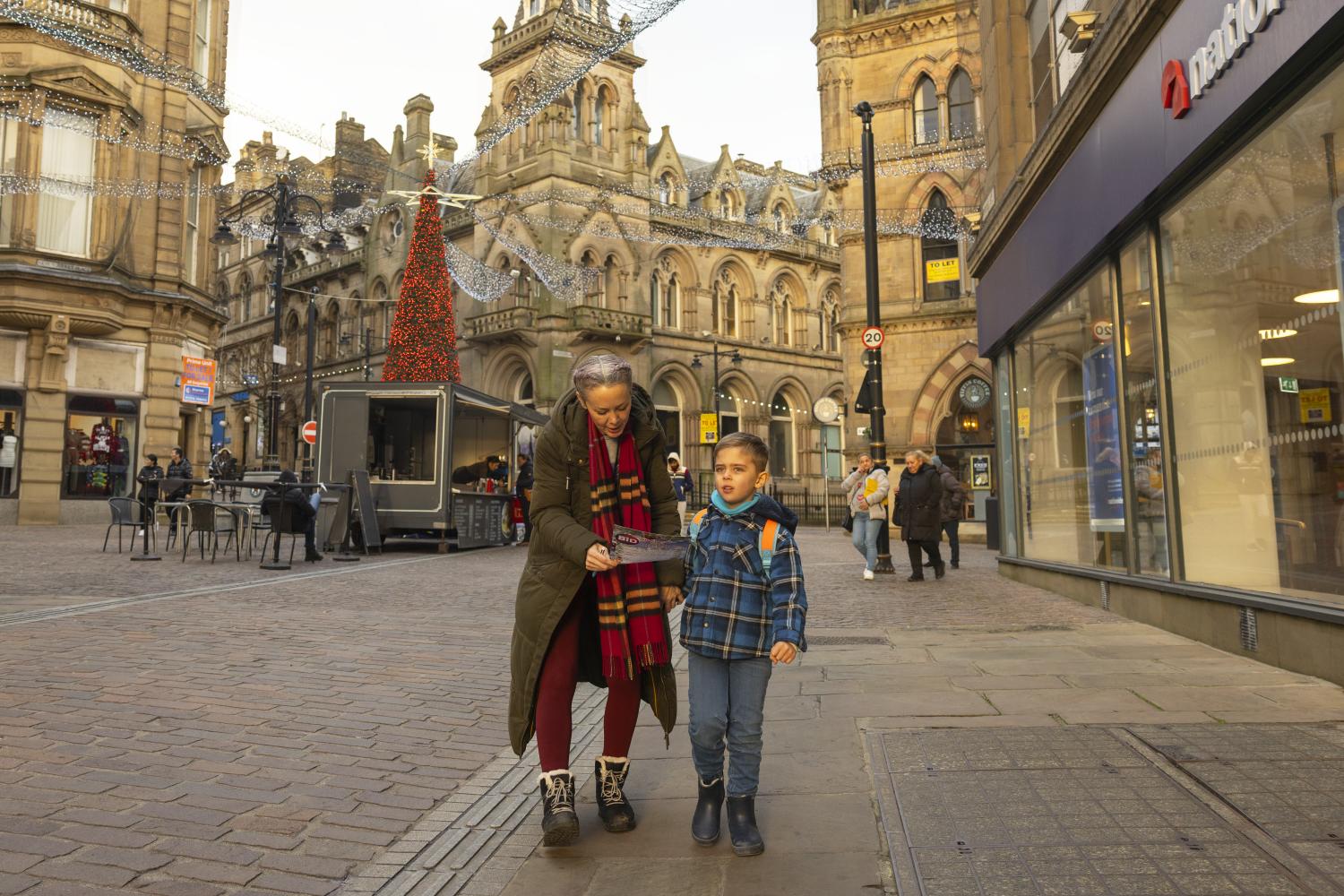 A woman and child walking along a paved street in Liverpool and looking at a map, with buildings and people in the background