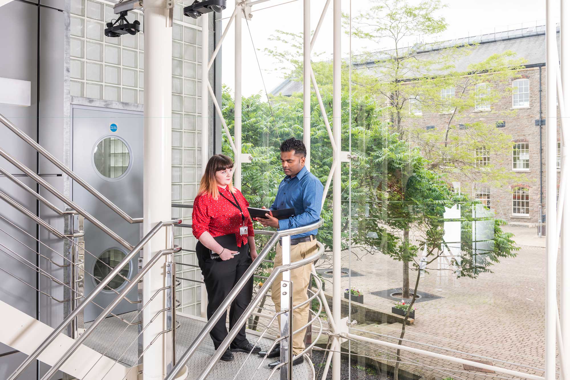 Interior view of the Historic England archive building, showing two staff members in conversation on a staircase landing.