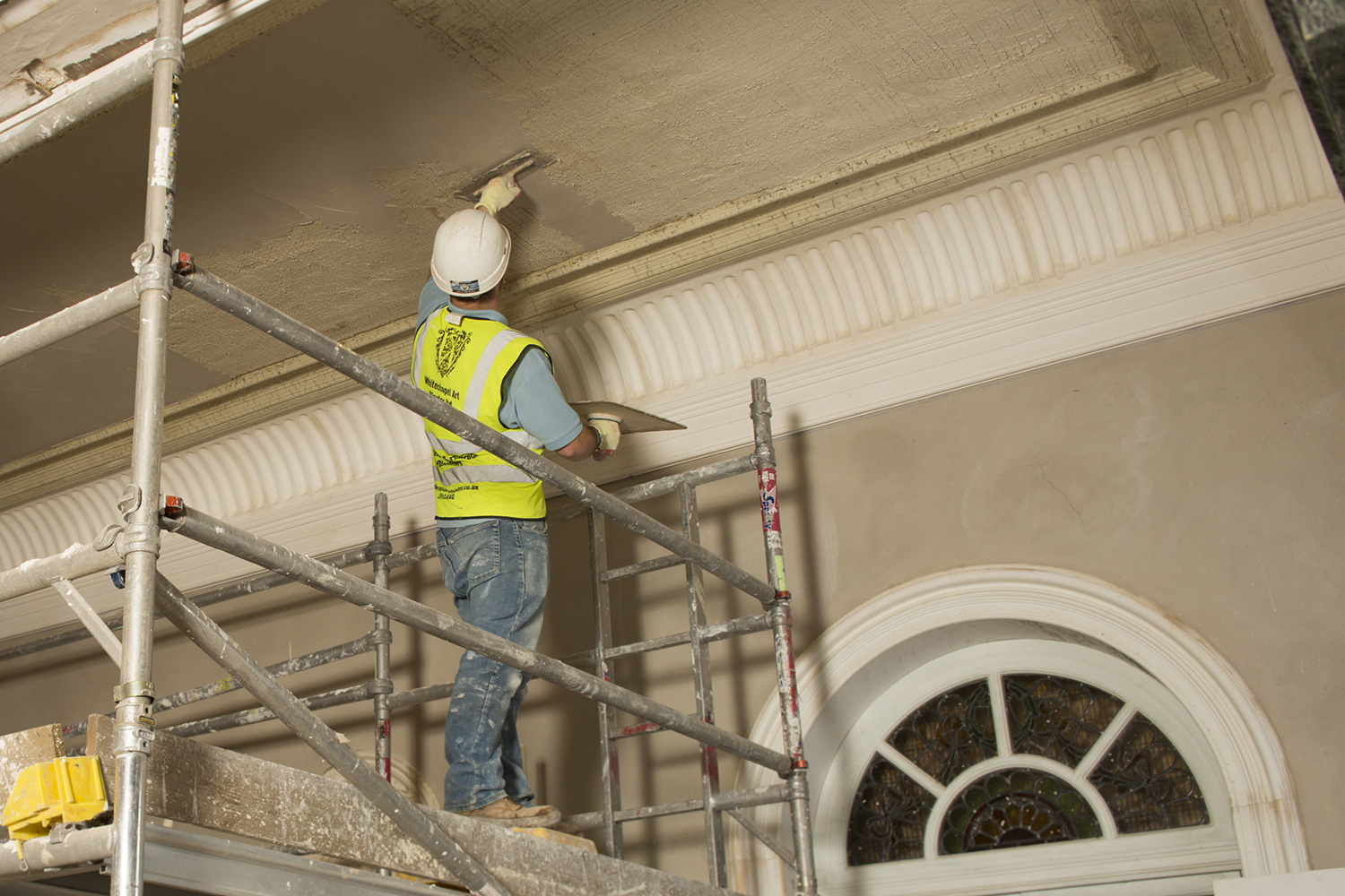 A worker on a scaffold applies plaster to a vaulted ceiling