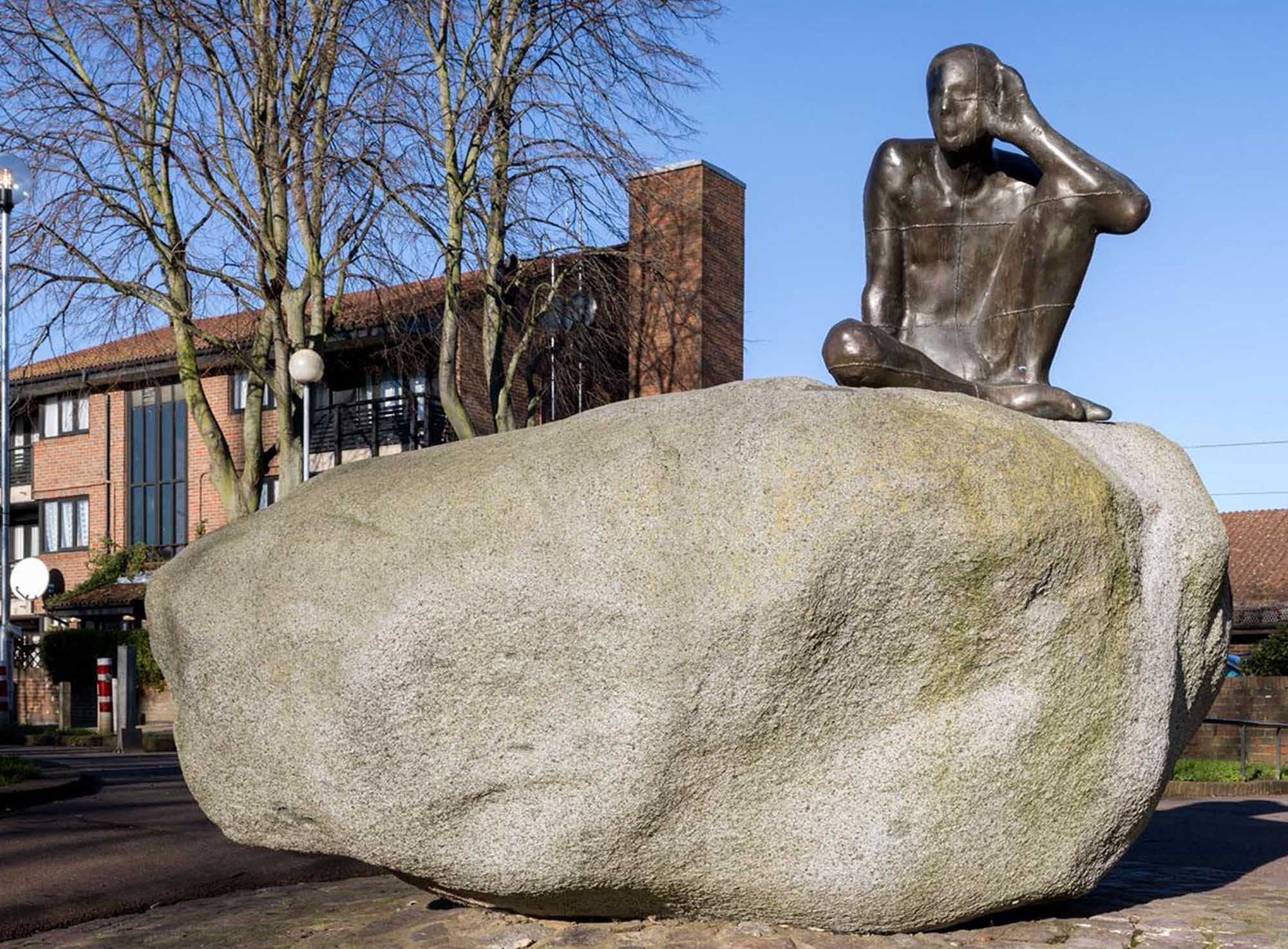 Sculpture of man sitting on a stone with his hand to his ear