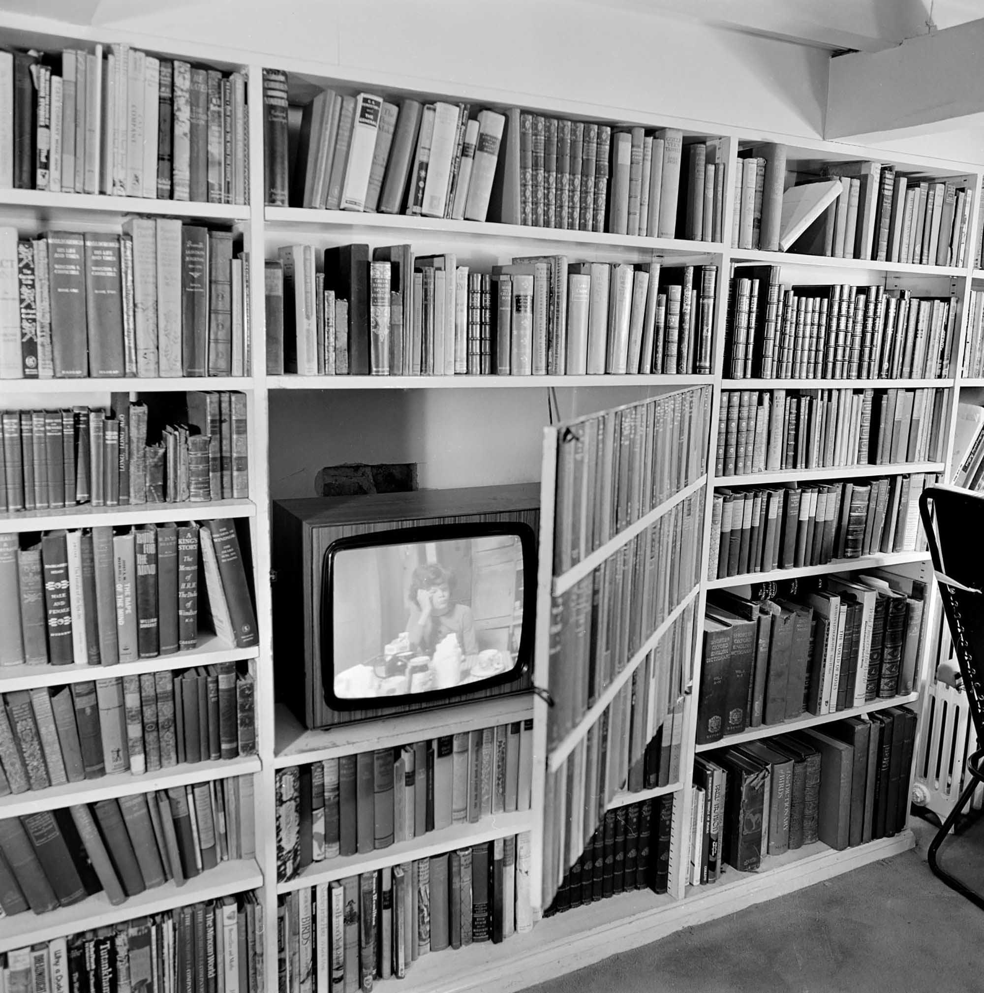Black and white photo of a television in a bookcase.