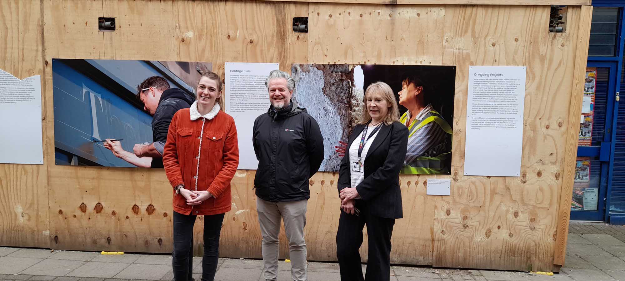 Two women and a man standing in front of a boarded up building.