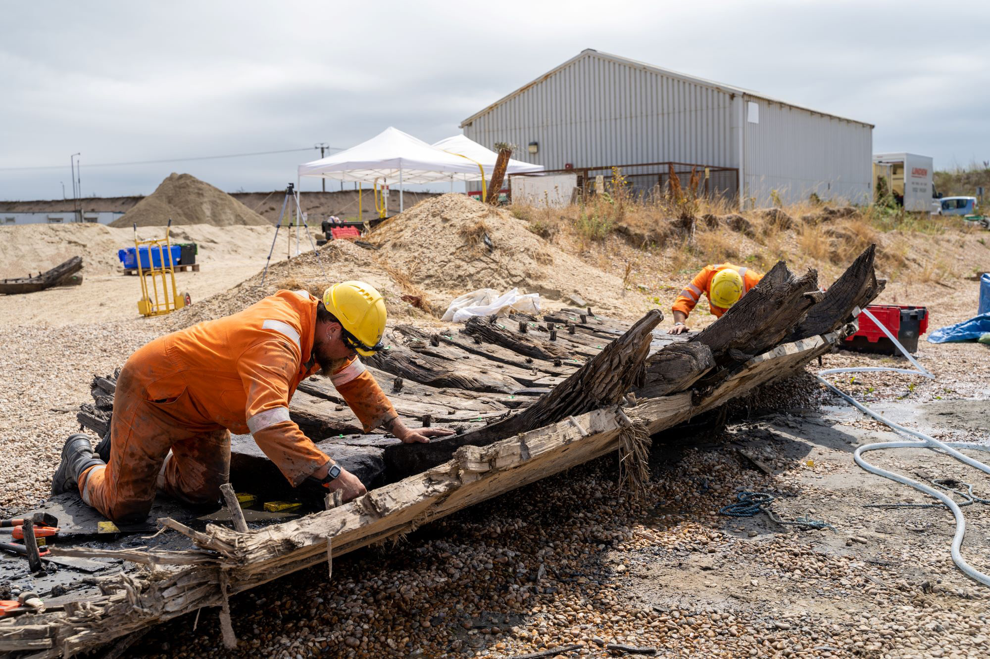 Two men in high visibility clothing kneel to investigate historic timbers on the ground