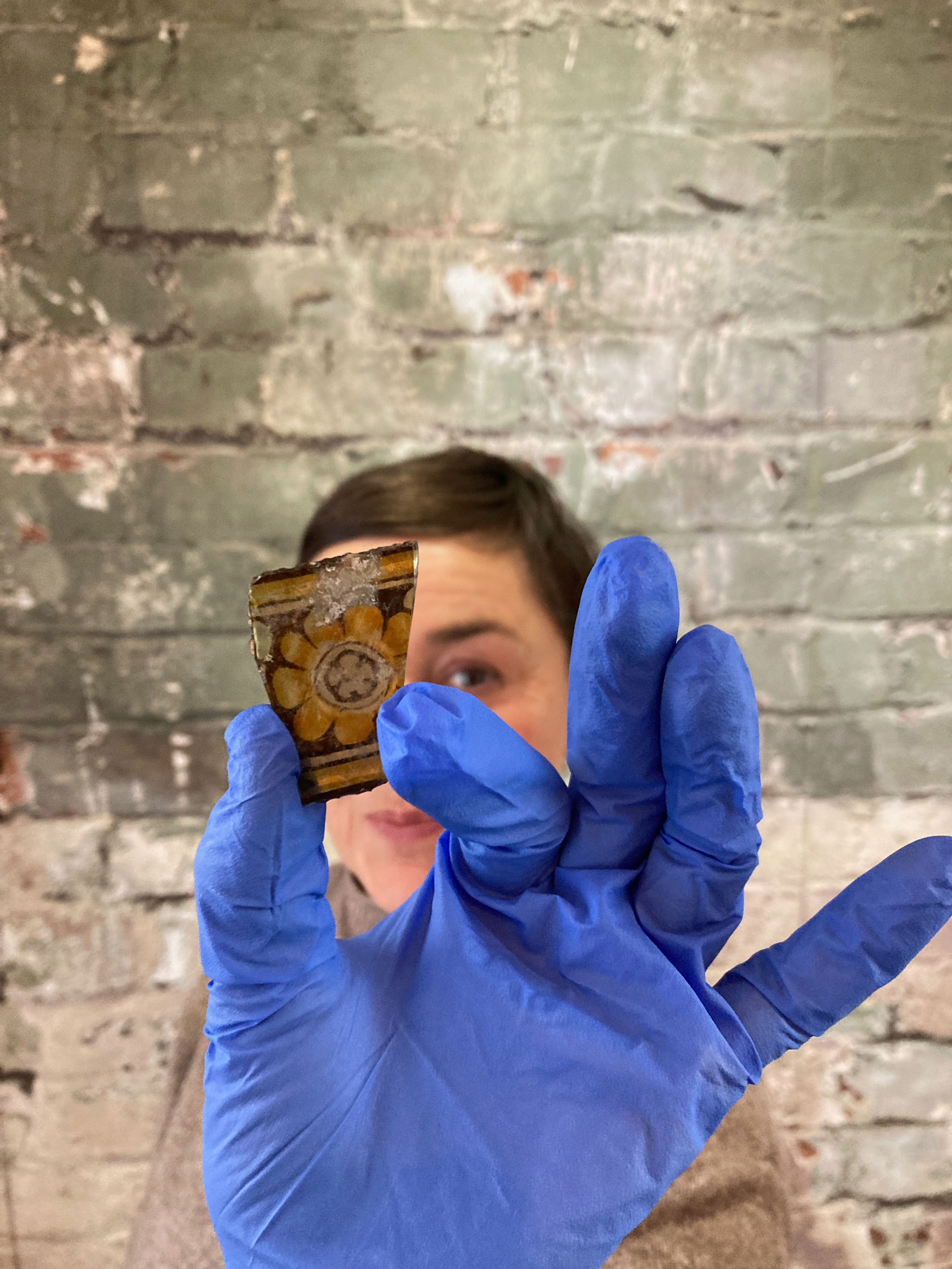 A woman holding up a small fragment of coloured glass which has a floral design on it.