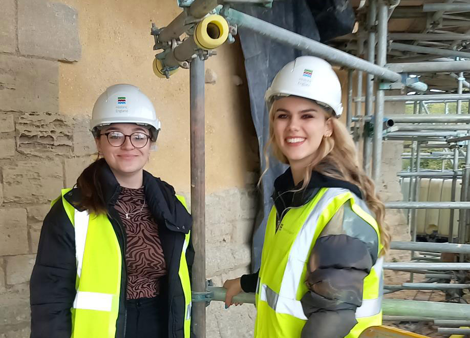 Two young women wearing PPE clothing standing on a scaffolding.