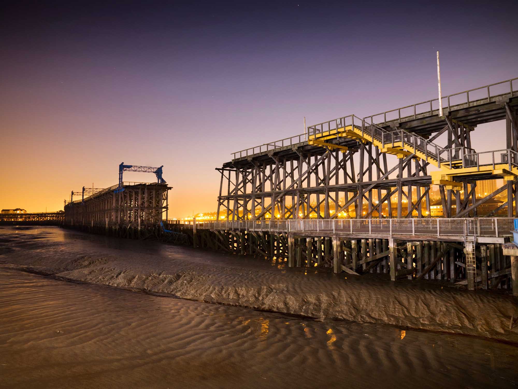 Landscape photograph of Dunston Staiths at sundown. The tide is out and the sky is purple and orange.