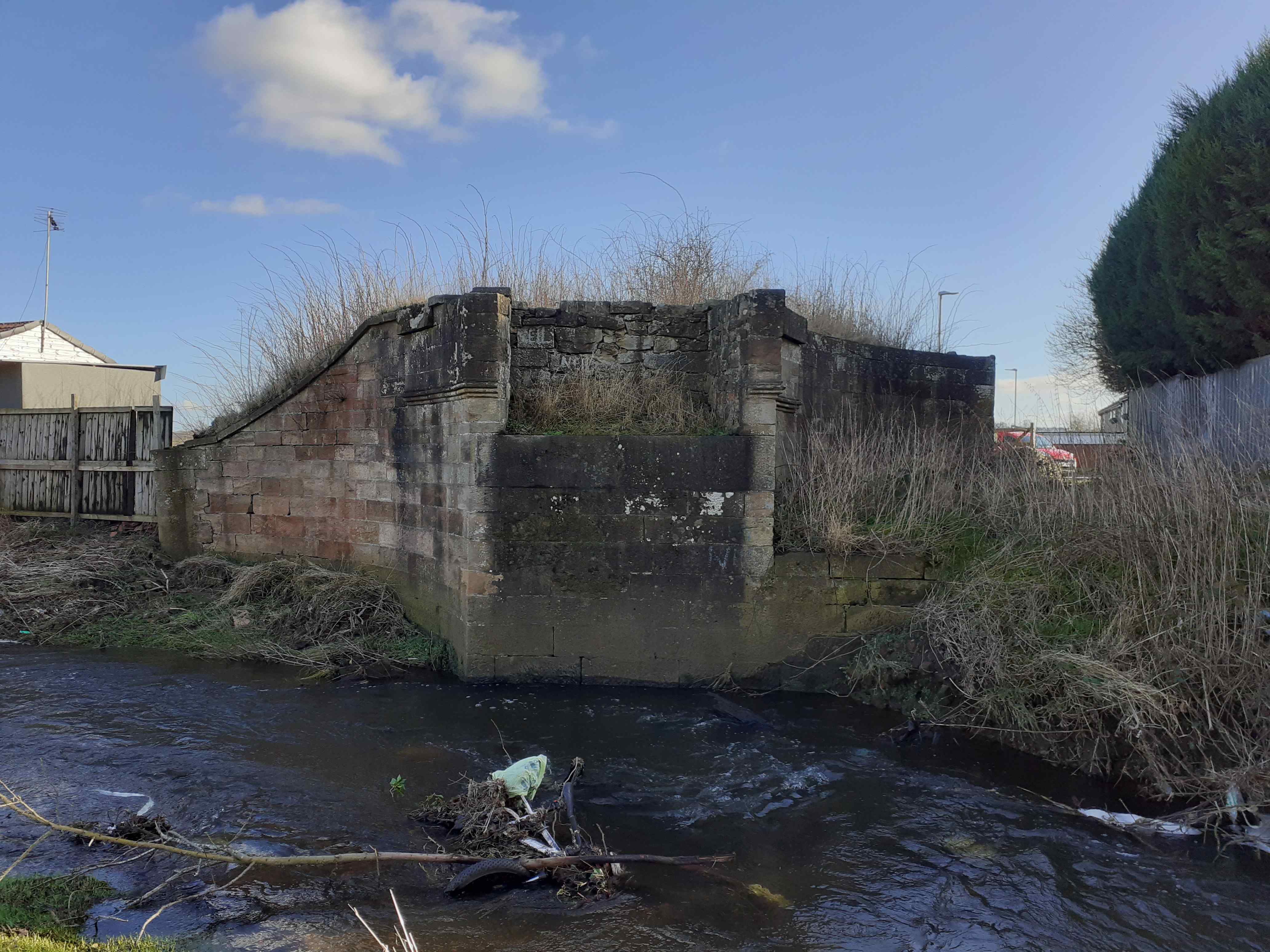 The remains of a stone bridge abutment next to a narrow river. 